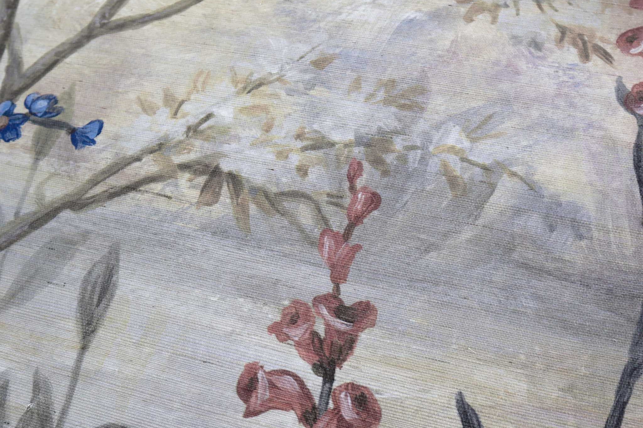 Close-up of a hand-painted floral mural on textured grasscloth wallpaper, featuring soft hues of grey, peach, and blue.
