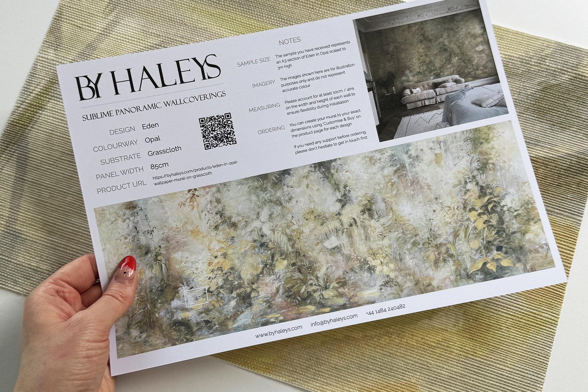 A hand showing information for a grasscloth wallpaper mural sample which features an abstract forest in lemon and cream.
