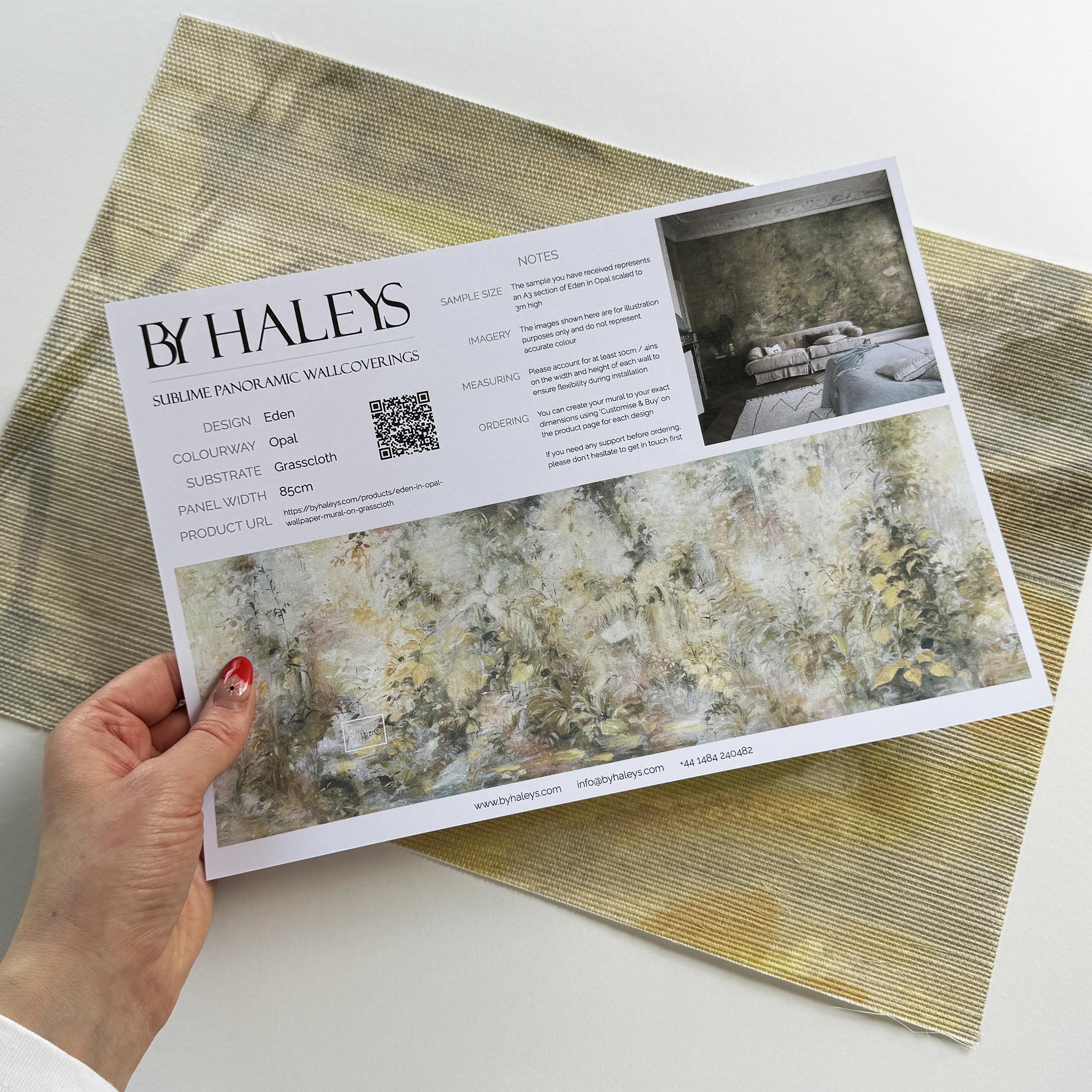 A hand showing information for a grasscloth wallpaper mural sample which features an abstract forest in lemon and cream.