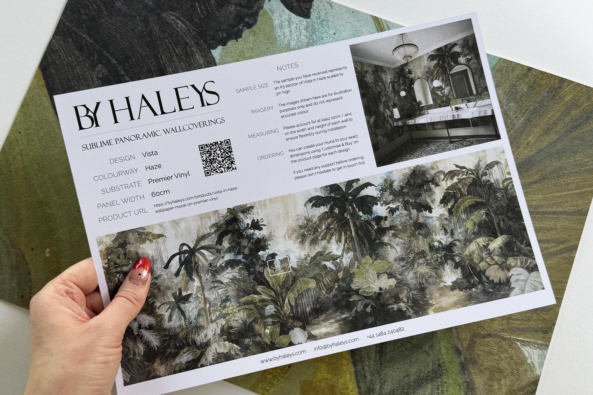 A hand showing information for a vinyl wallpaper mural sample which features a tropical scene in sage and parchment.