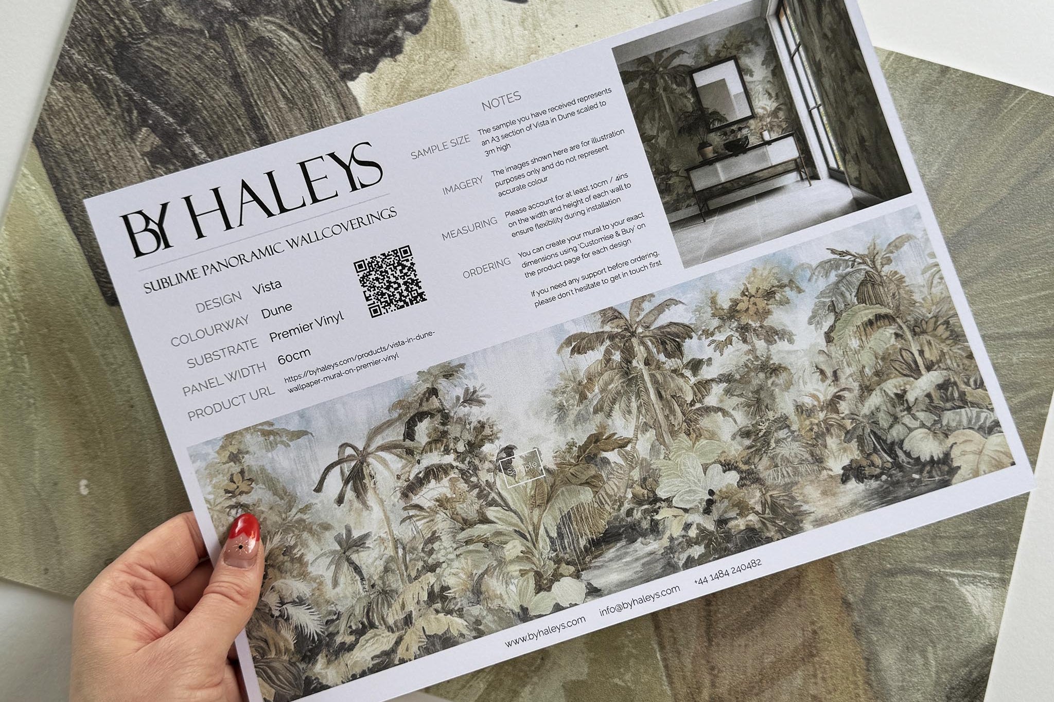 A hand showing information for a vinyl wallpaper mural sample which features a jungle scene in sepia and blue.