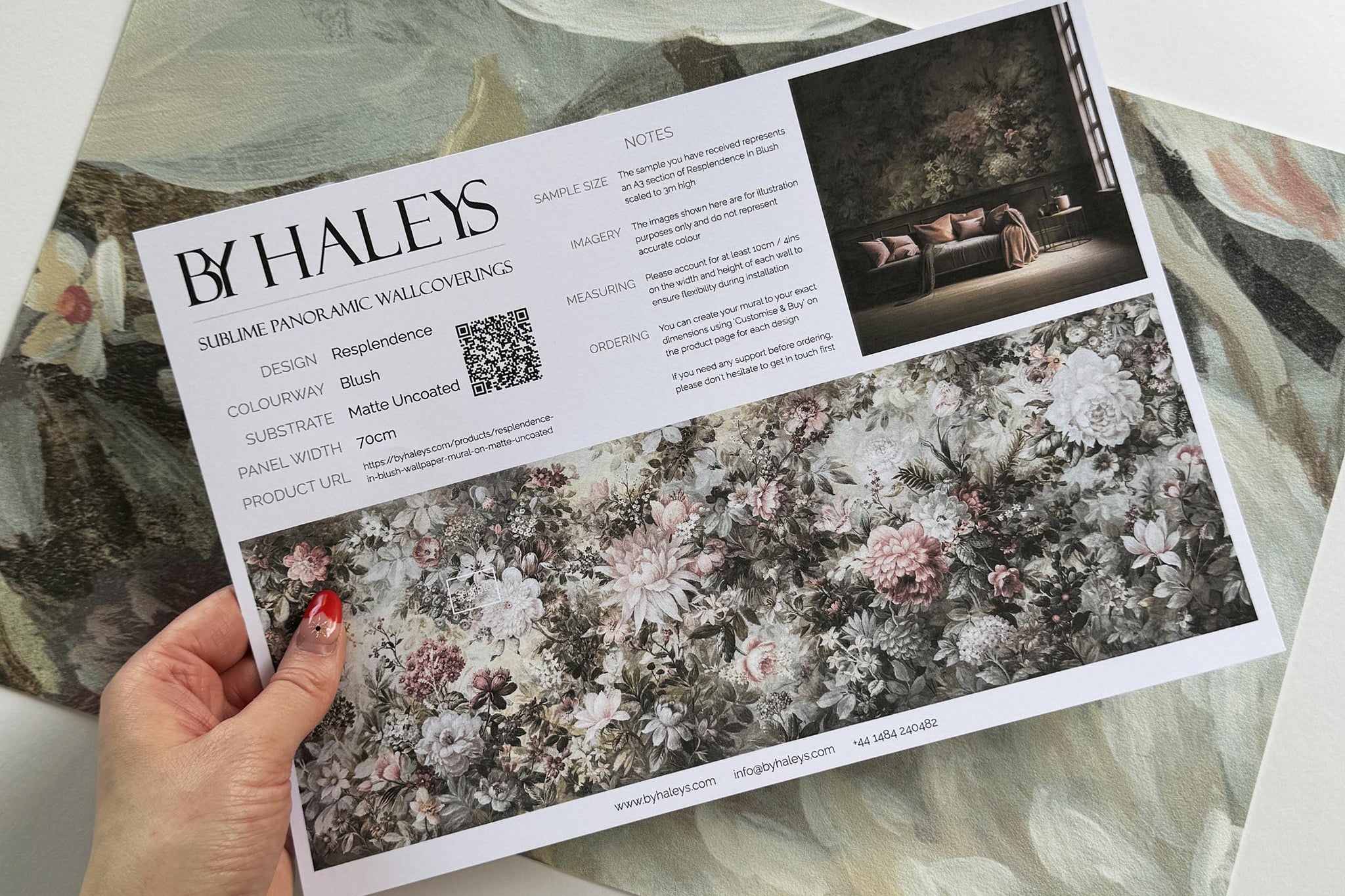A hand showing information for a vinyl wallpaper mural sample which features a floral composition in soft neutrals.