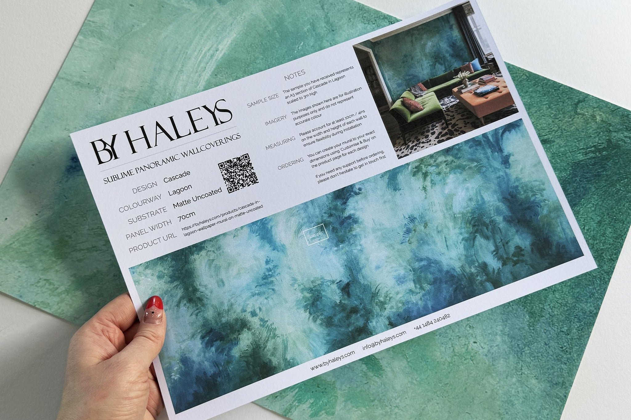 A hand showing information for a matte wallpaper mural sample which features an abstract wash in aqua and jade.