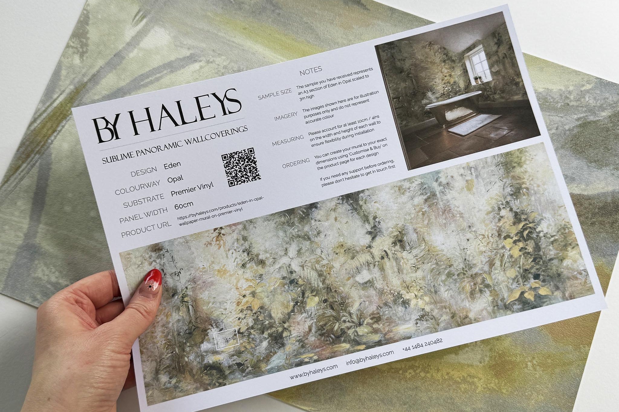 A hand showing information for a vinyl wallpaper mural sample which features an abstract forest in lemon and cream.
