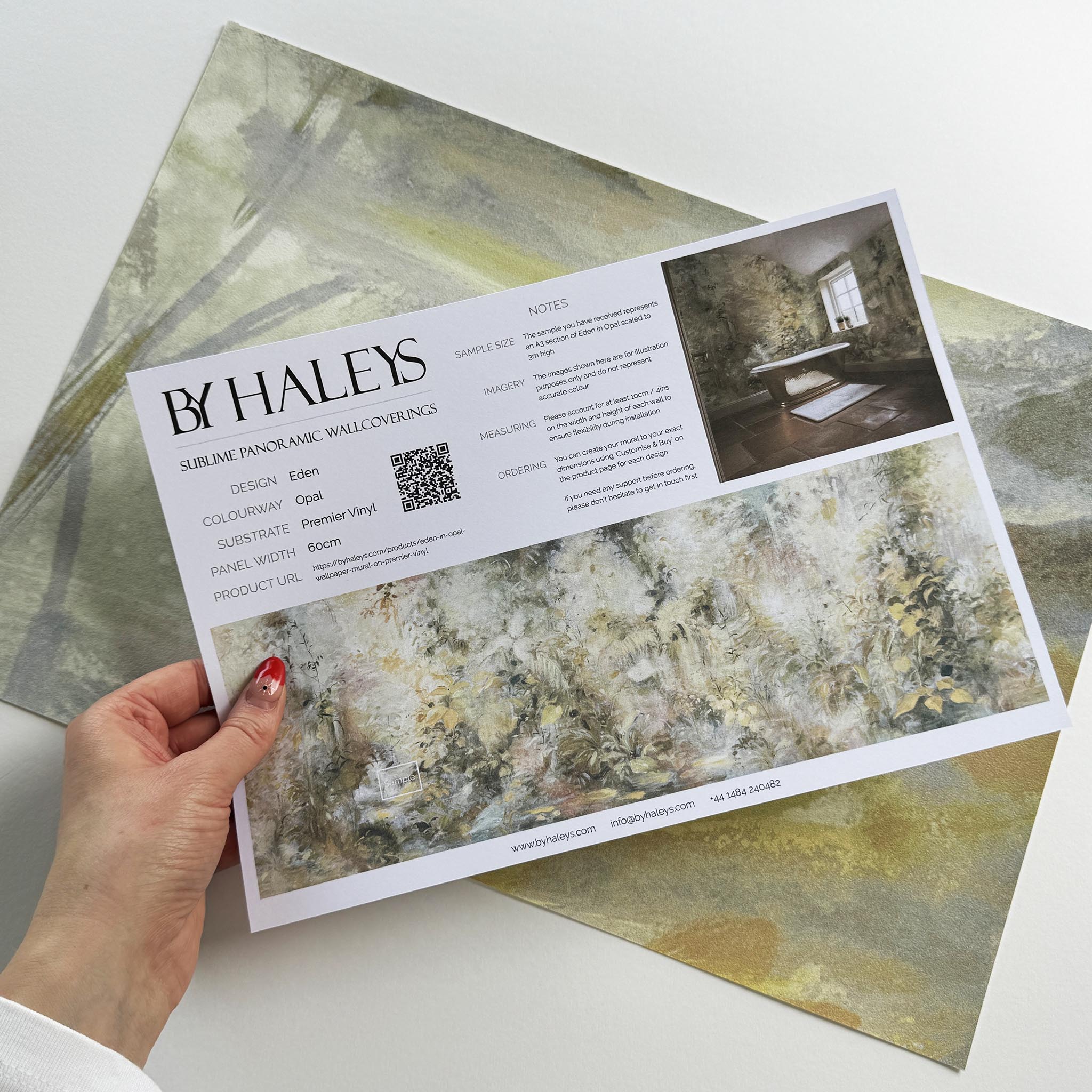 A hand showing information for a vinyl wallpaper mural sample which features an abstract forest in lemon and cream.
