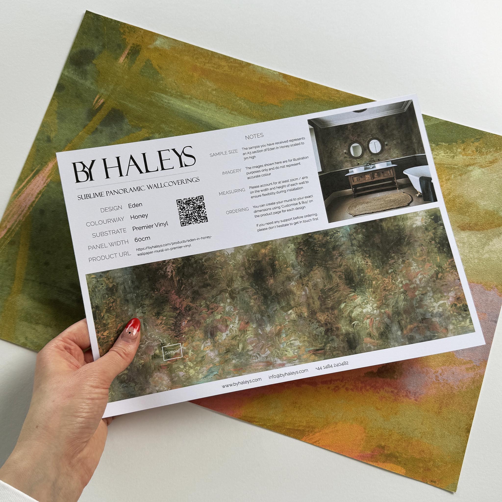 A hand showing information for a vinyl wallpaper mural sample which features a abstract layering of ochre and teal.
