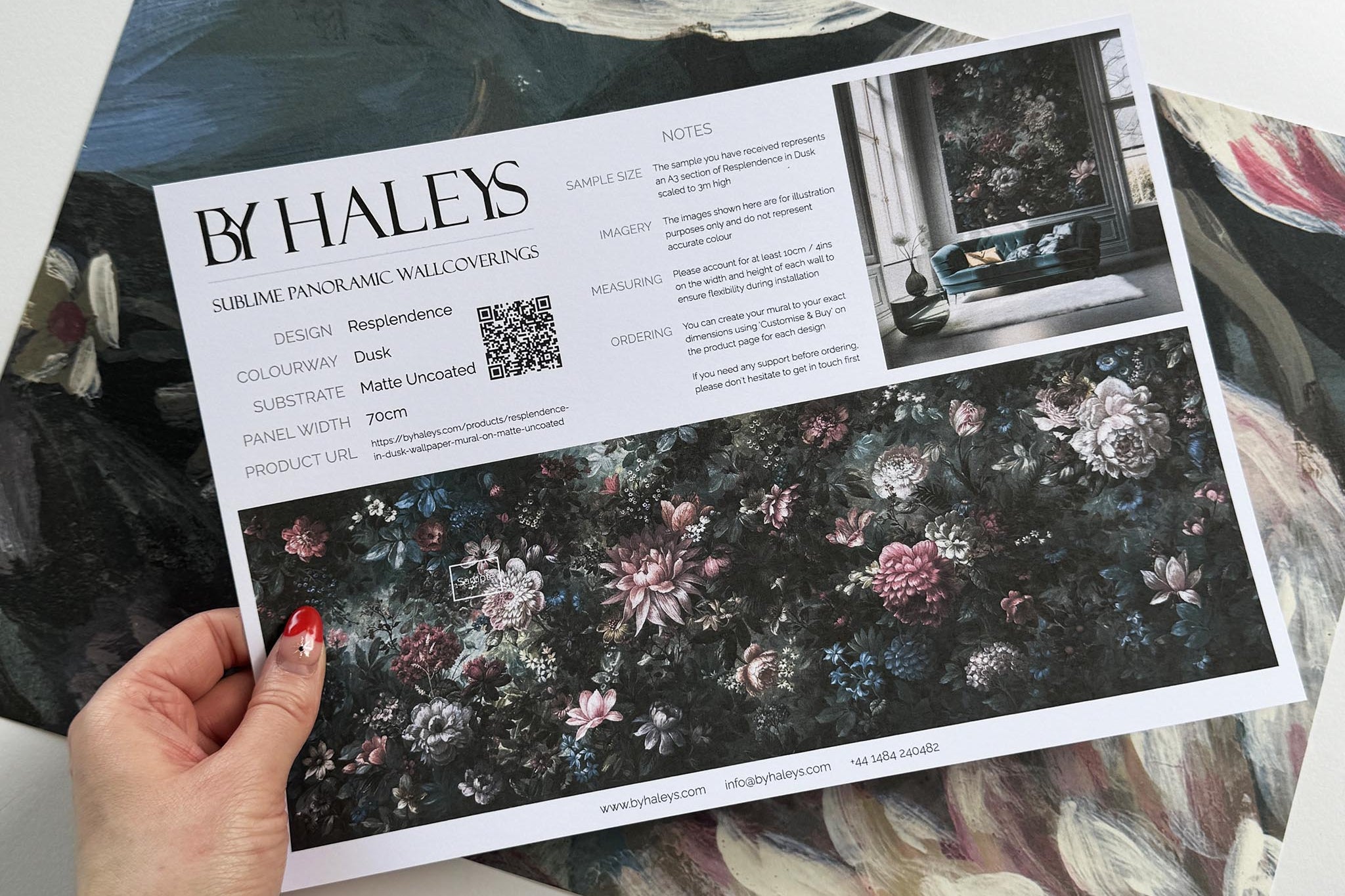 A hand showing information for a matte wallpaper mural sample which features a floral bloom in crimson and blue.