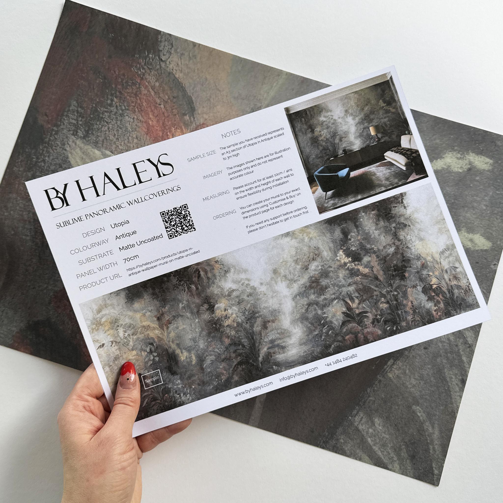 A hand showing information for a matte wallpaper mural sample which features a rainforest in lavender and rust.