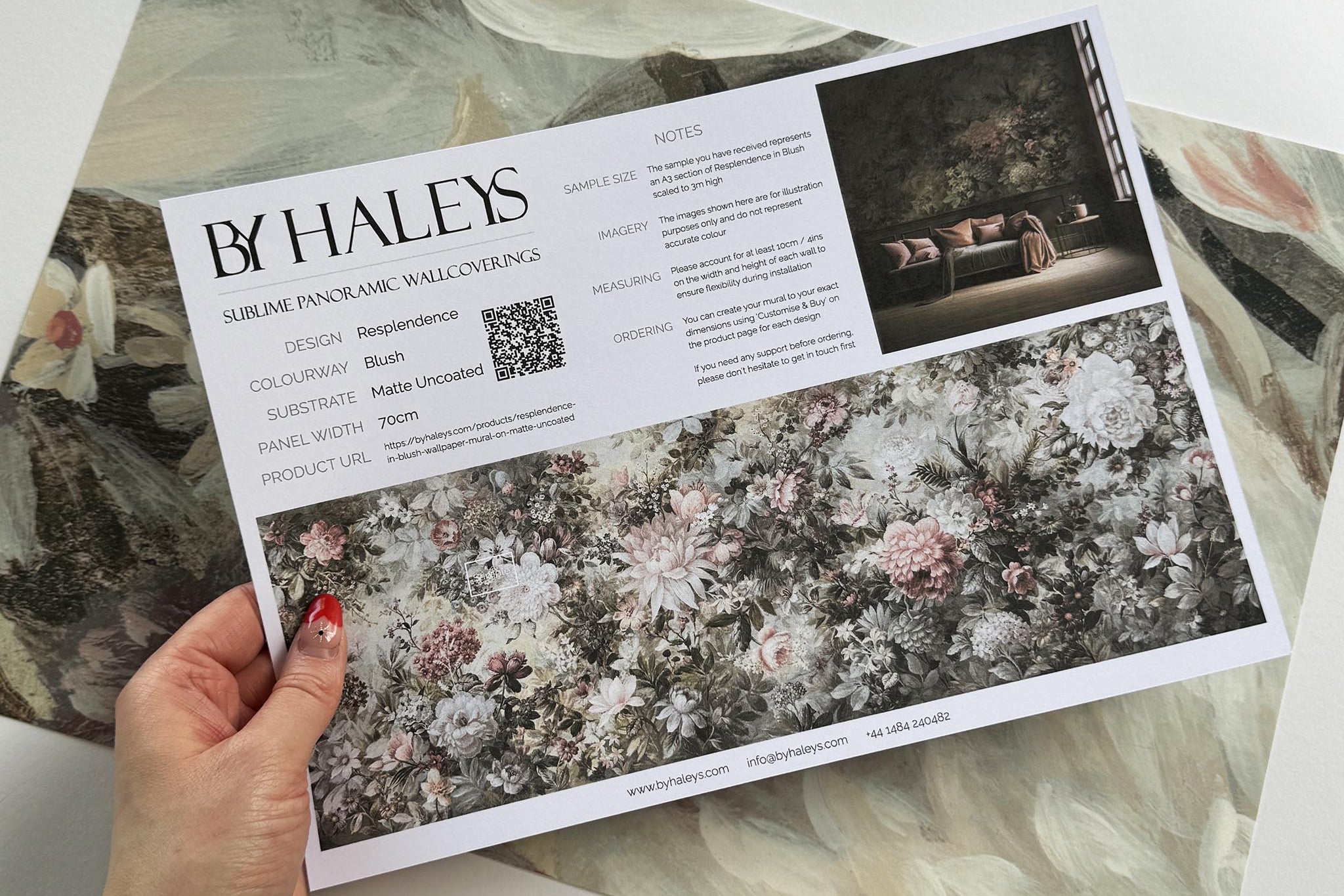A hand showing information for a matte wallpaper mural sample which features a floral composition in soft neutrals.