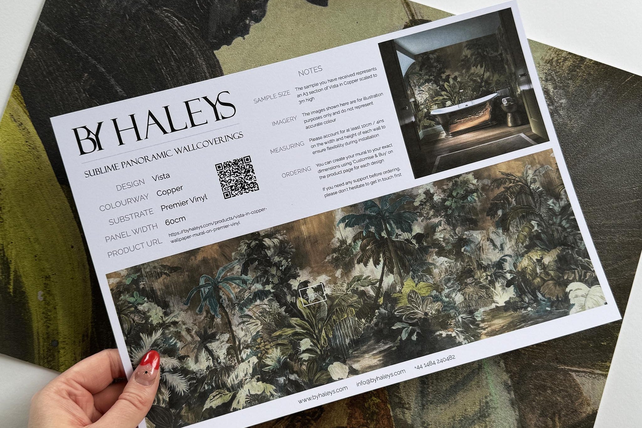 A hand showing information for a vinyl wallpaper mural sample which features a moody jungle in teal and ochre.