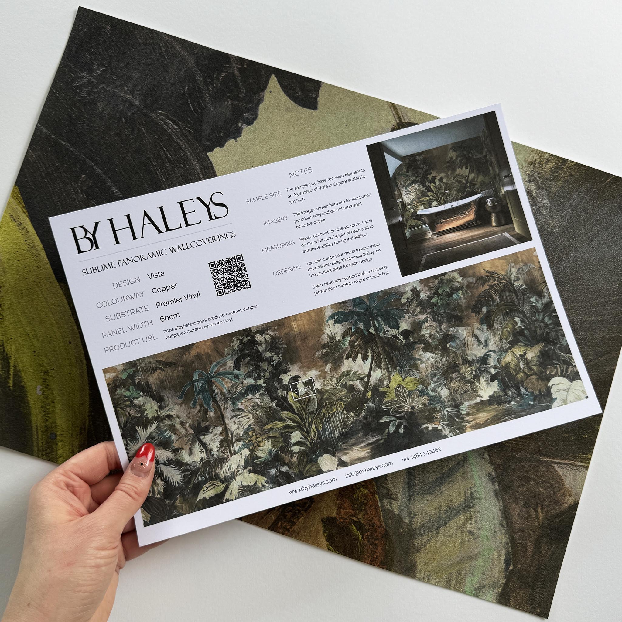 A hand showing information for a vinyl wallpaper mural sample which features a moody jungle in teal and ochre.