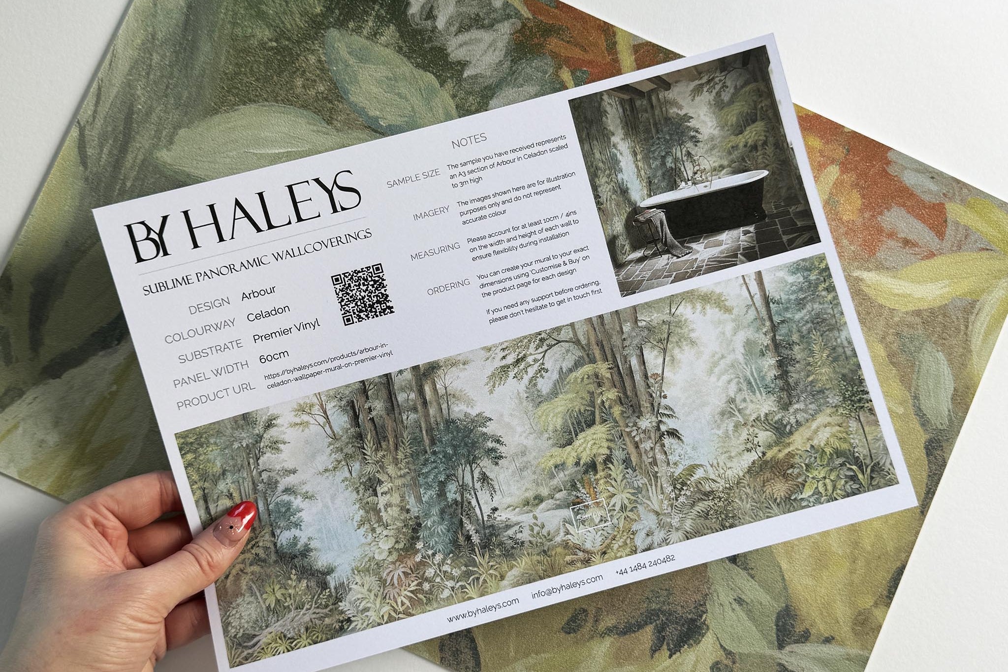 A hand showing information for a vinyl wallpaper mural sample which features an airy woodland in sage, yellow, and mist.