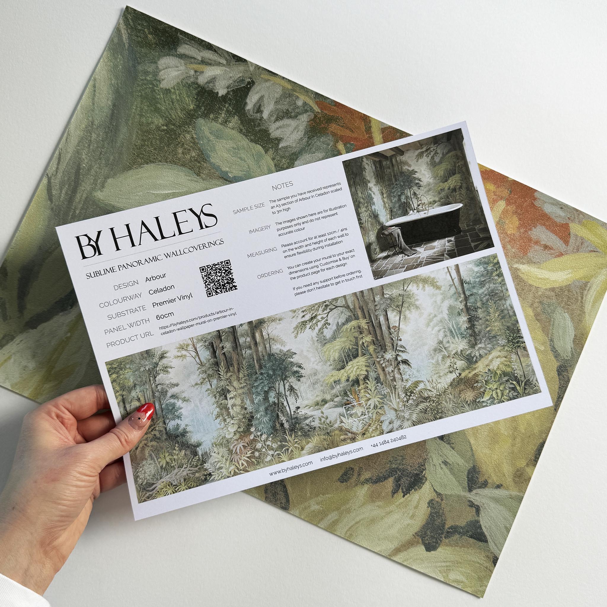 A hand showing information for a vinyl wallpaper mural sample which features an airy woodland in sage, yellow, and mist.