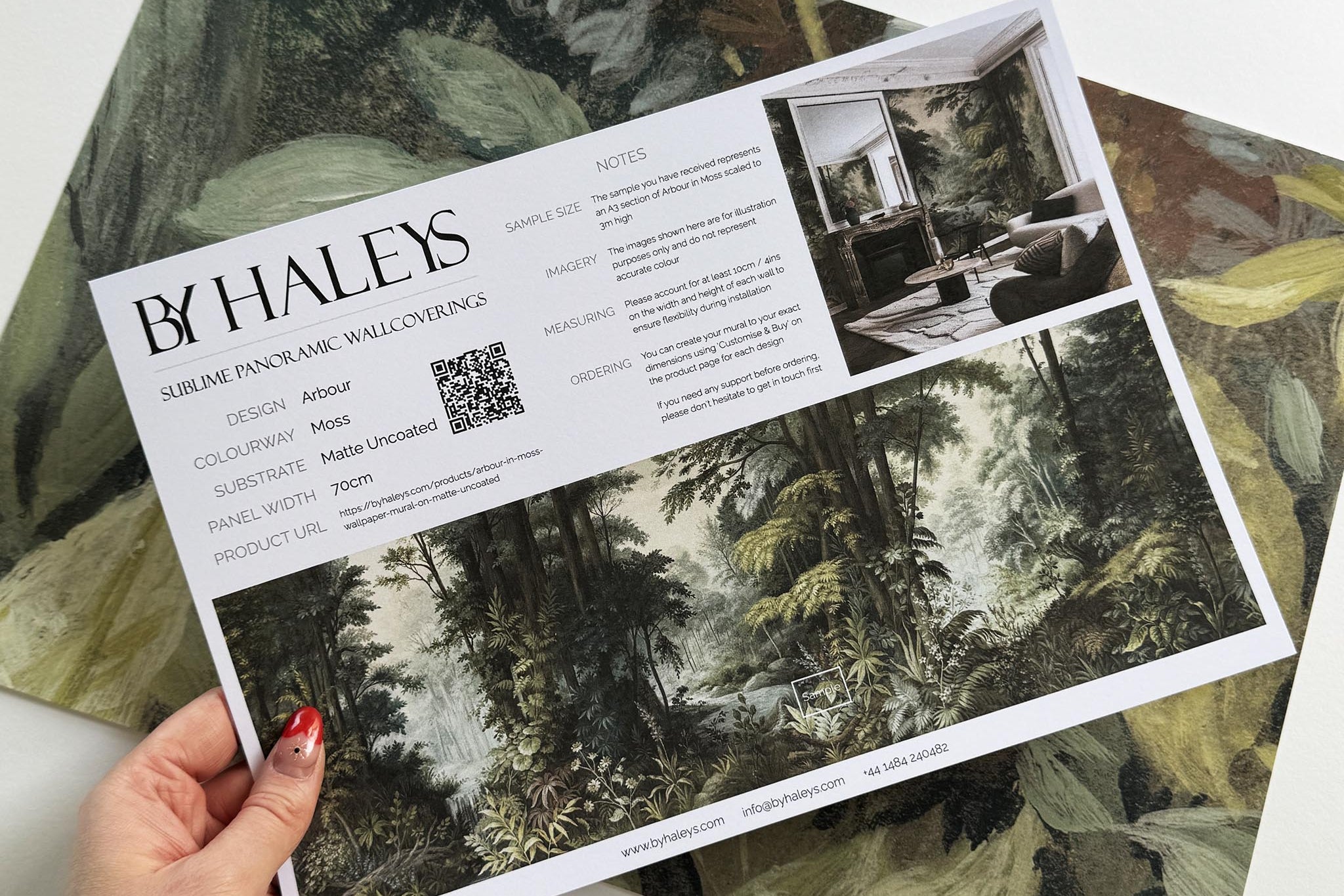 A hand showing information for a matte wallpaper mural sample which features a misty woodland in sage and ochre.