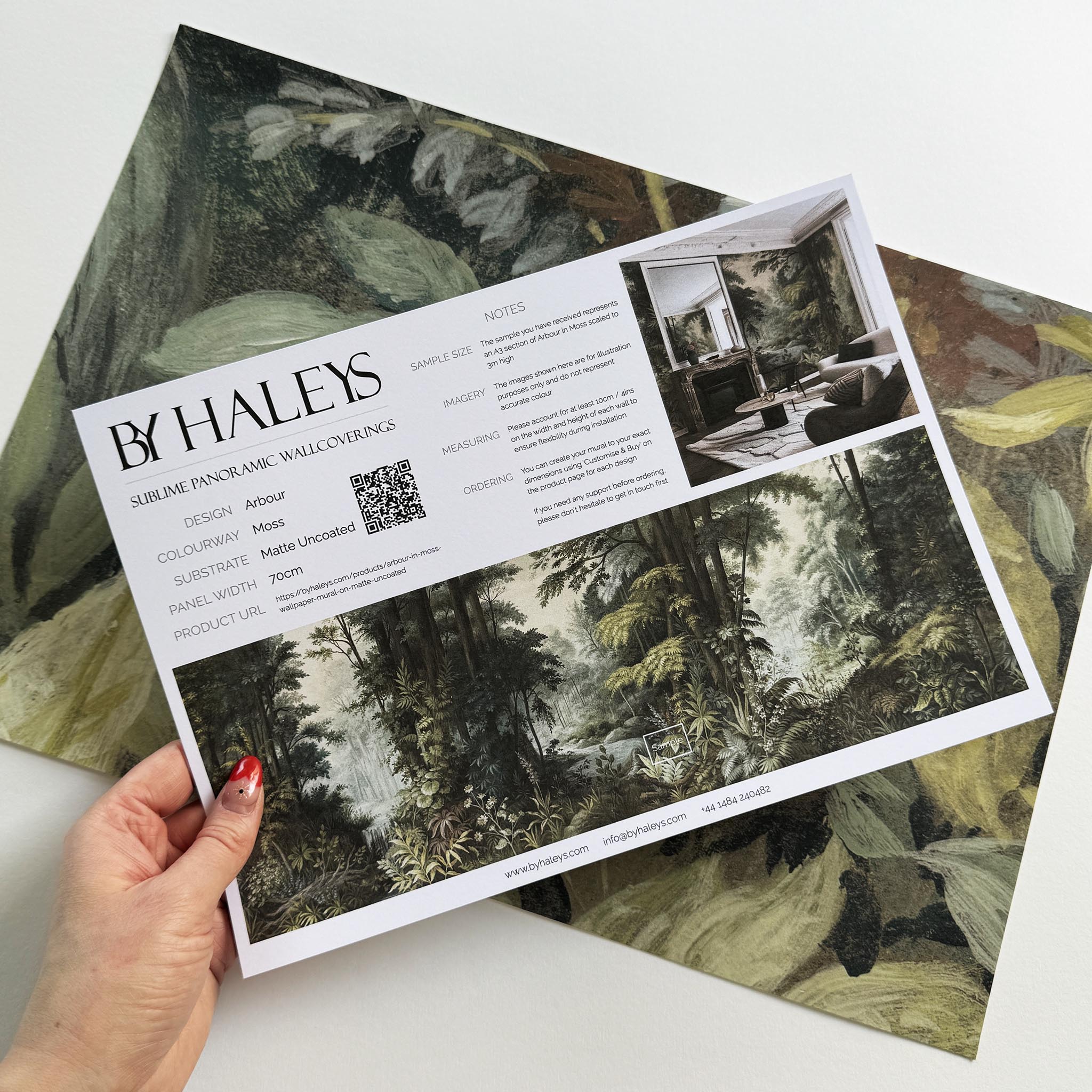 A hand showing information for a matte wallpaper mural sample which features a misty woodland in sage and ochre.