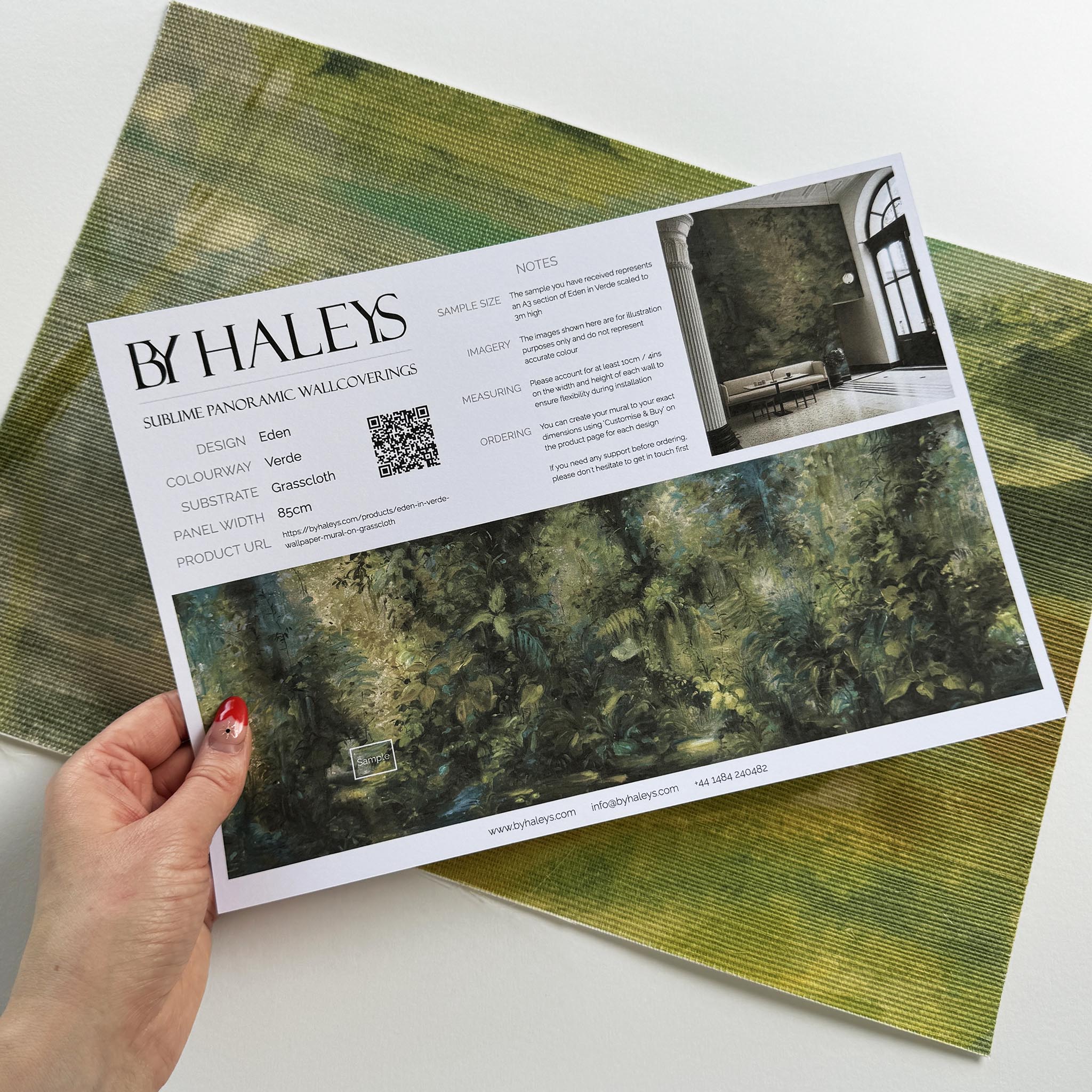 A hand showing information for a grasscloth wallpaper mural sample which features a jungle abstraction in emerald and ochre.