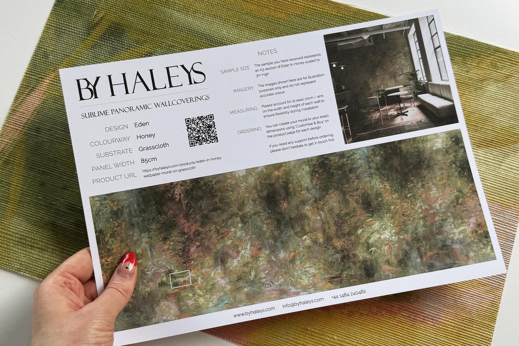 A hand showing information for a grasscloth wallpaper mural sample which features a abstract layering of ochre and teal.