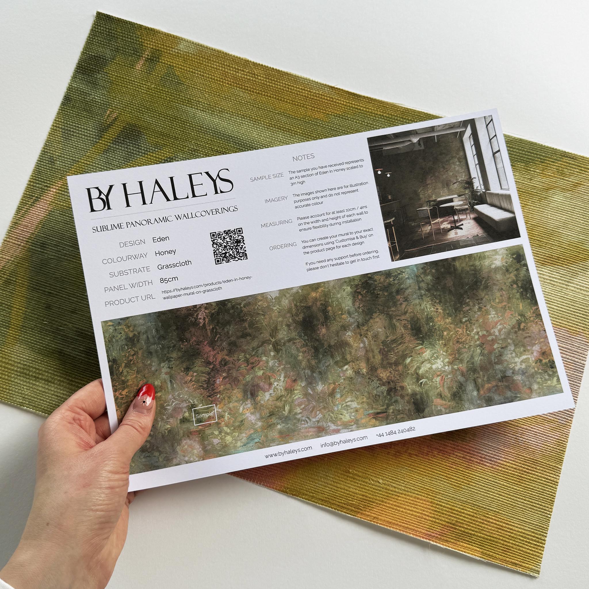 A hand showing information for a grasscloth wallpaper mural sample which features a abstract layering of ochre and teal.