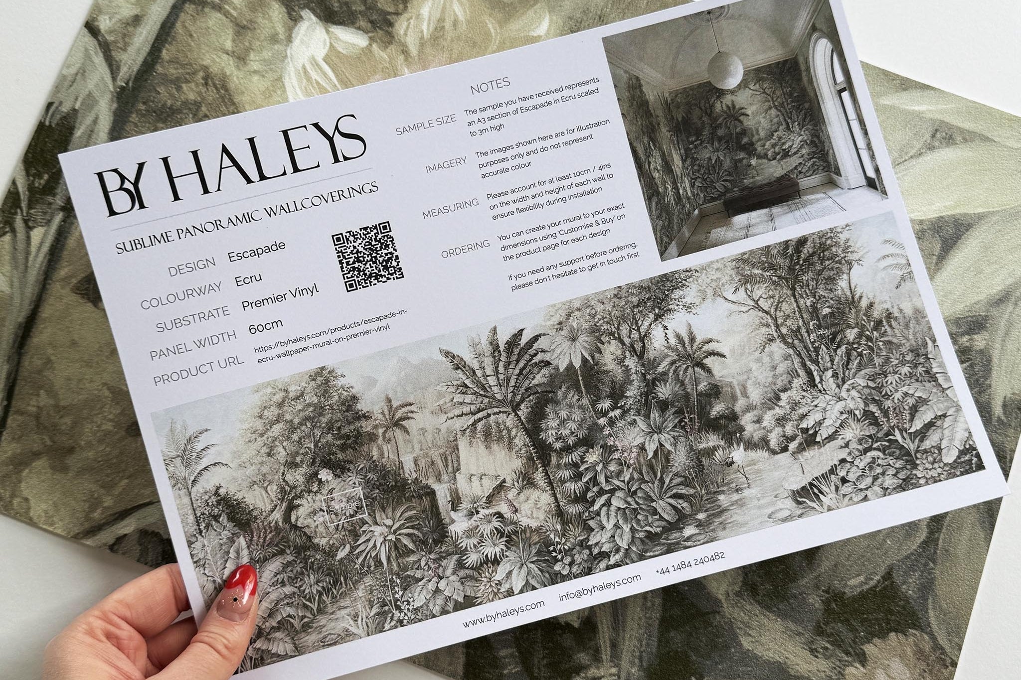 A hand showing information for a vinyl wallpaper mural sample which features a jungle vista in sepia and blush.