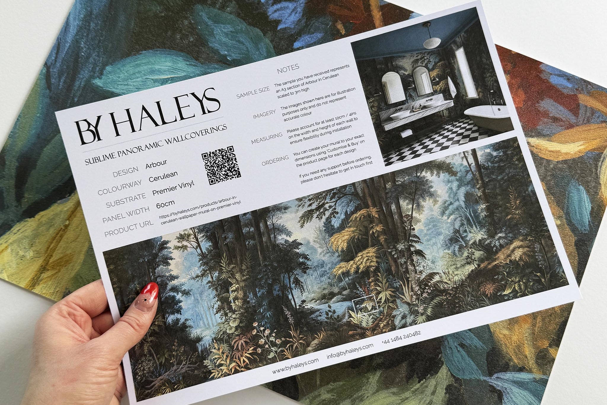 A hand showing information for a vinyl wallpaper mural sample which features an enchanted forest in blue and rust.