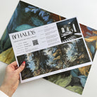 A hand showing information for a vinyl wallpaper mural sample which features an enchanted forest in blue and rust.