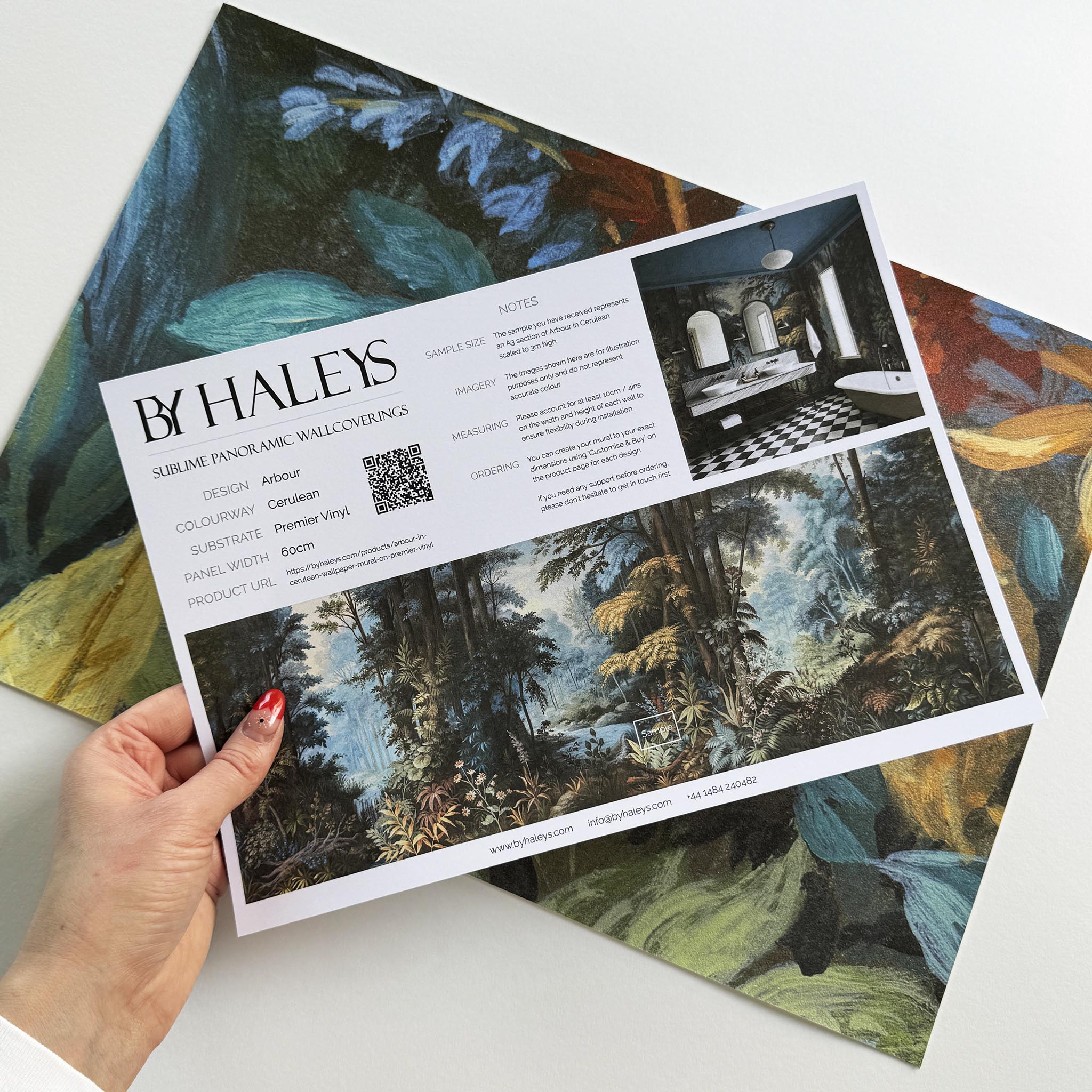 A hand showing information for a vinyl wallpaper mural sample which features an enchanted forest in blue and rust.
