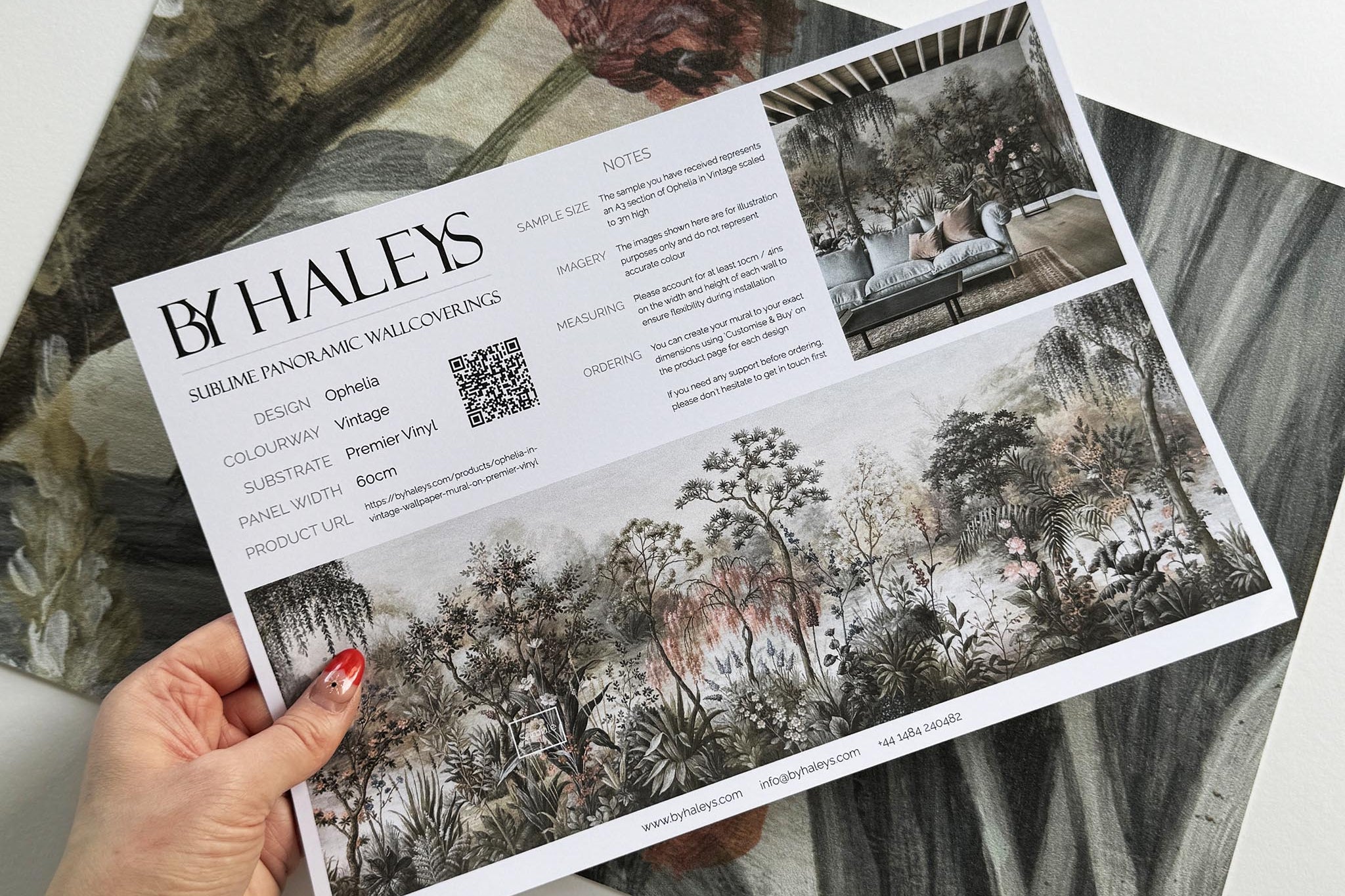 A hand showing information for a vinyl wallpaper mural sample which features a lakeside scene in vintage tones.