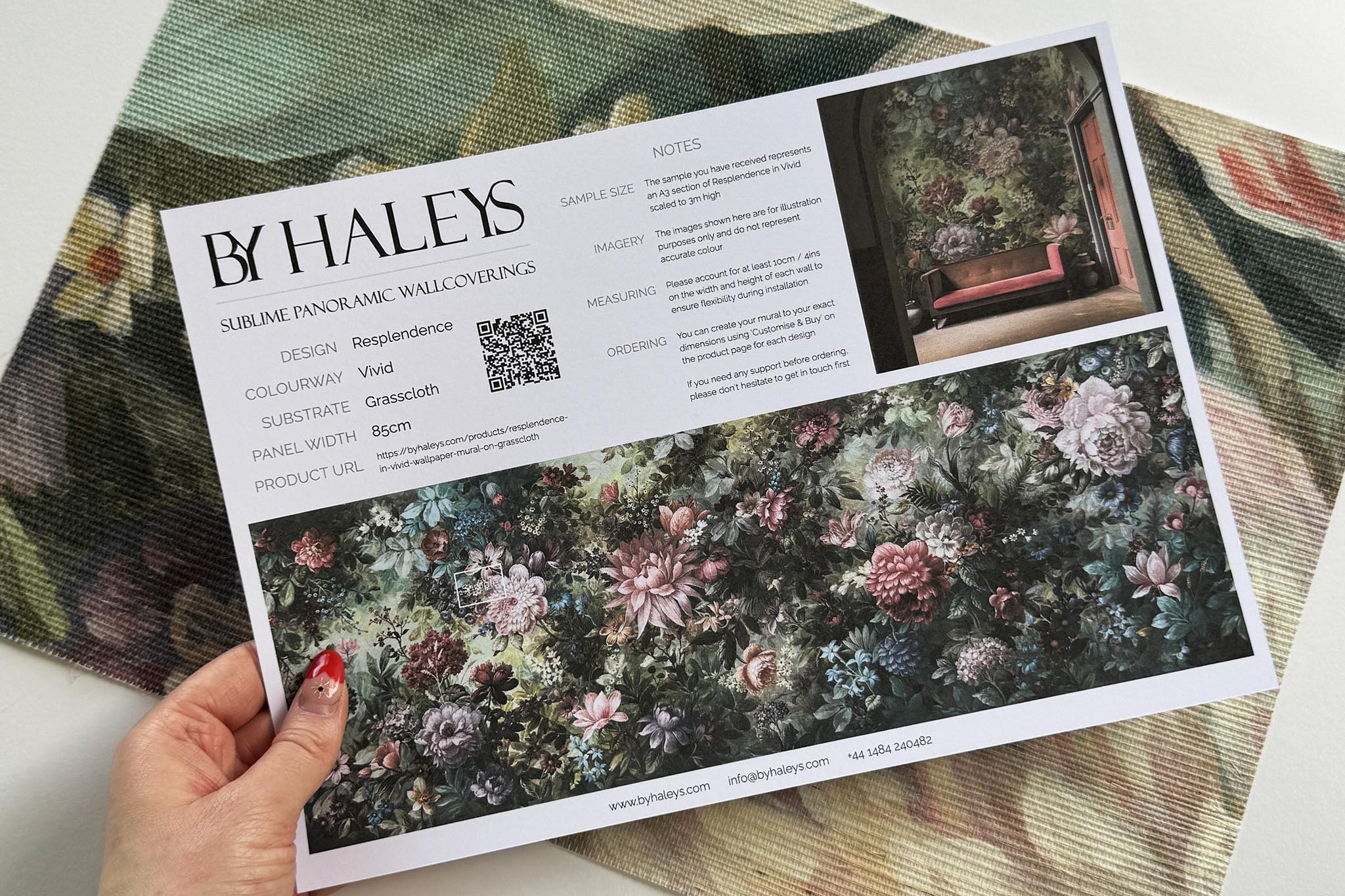 A hand showing information for a grasscloth wallpaper mural sample which features a floral tapestry in rich jewel tones.