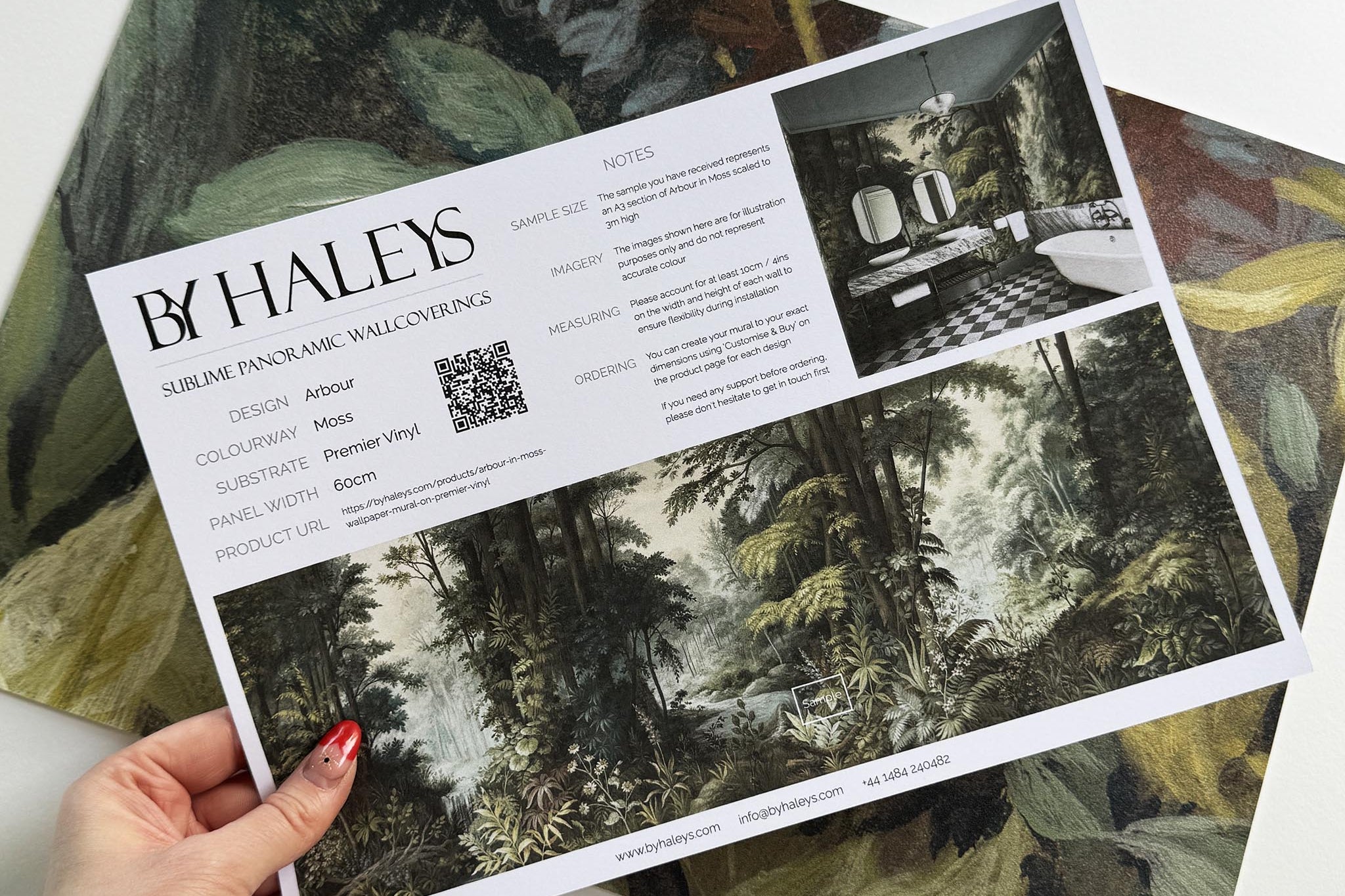 A hand showing information for a vinyl wallpaper mural sample which features a misty woodland in sage and ochre.