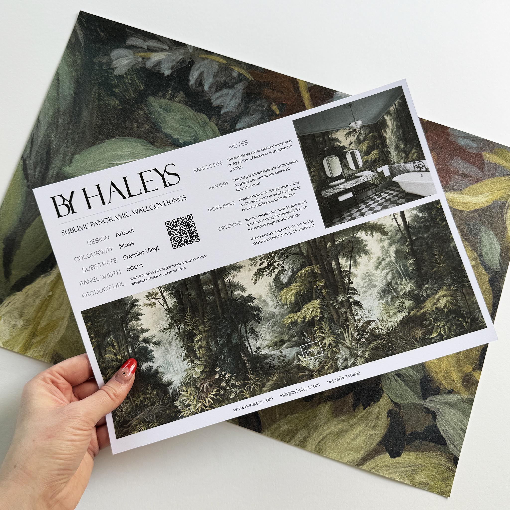 A hand showing information for a vinyl wallpaper mural sample which features a misty woodland in sage and ochre.