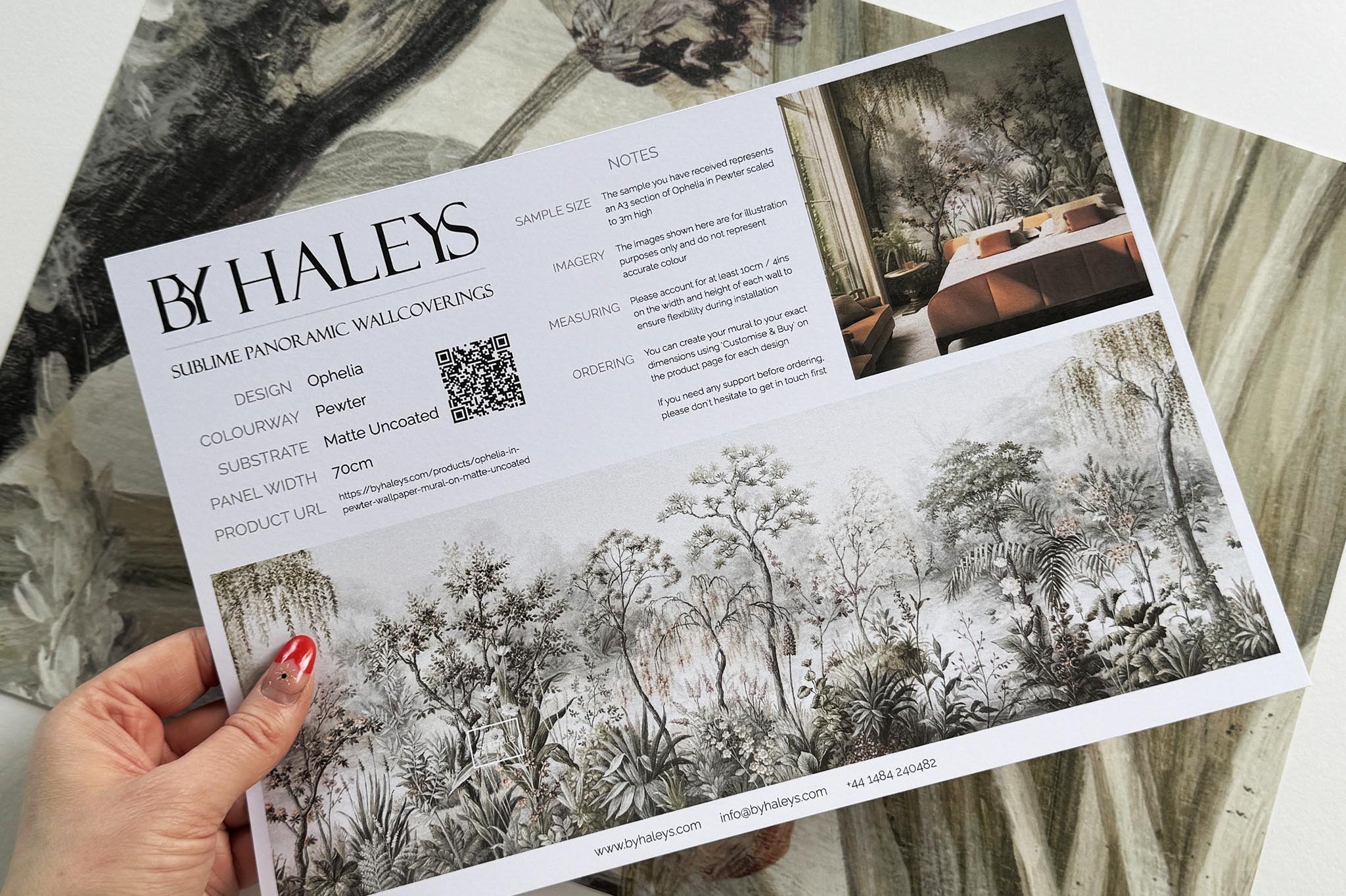 A hand showing information for a matte wallpaper mural sample which features a lakeside scene in grey and peach.