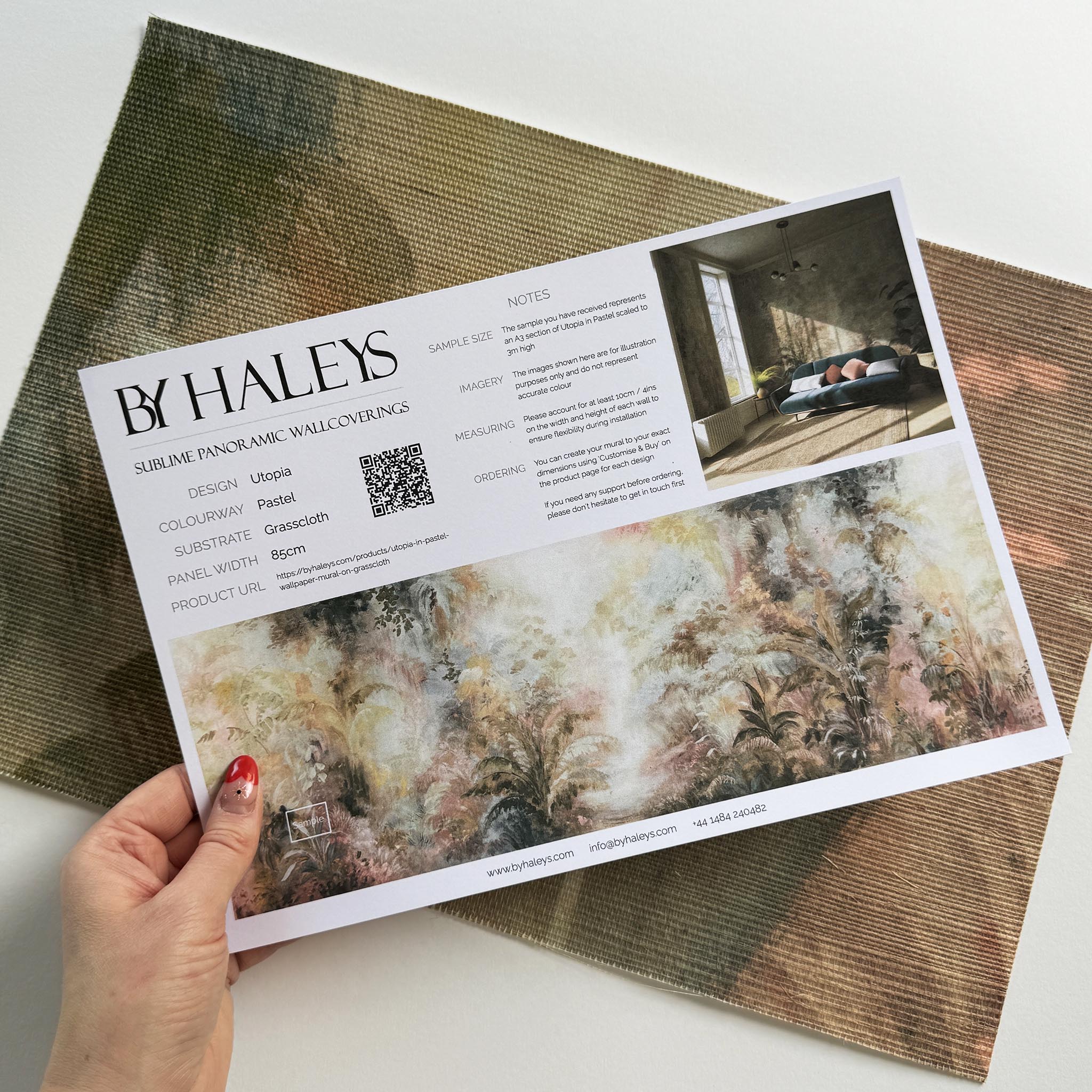 A hand showing information for a grasscloth wallpaper mural sample which features a rainforest in blush and sky blue.