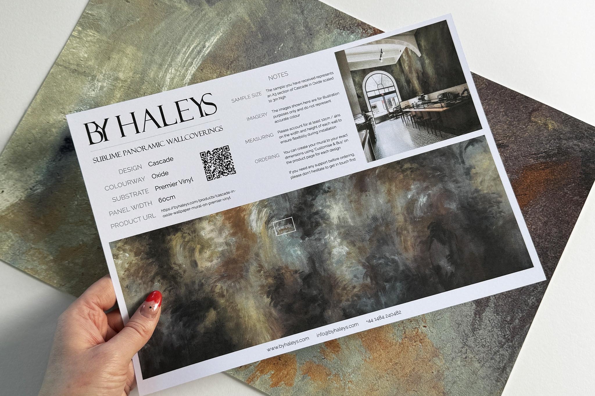 A hand showing information for a vinyl wallpaper mural sample which features an abstract haze in charcoal and ash.