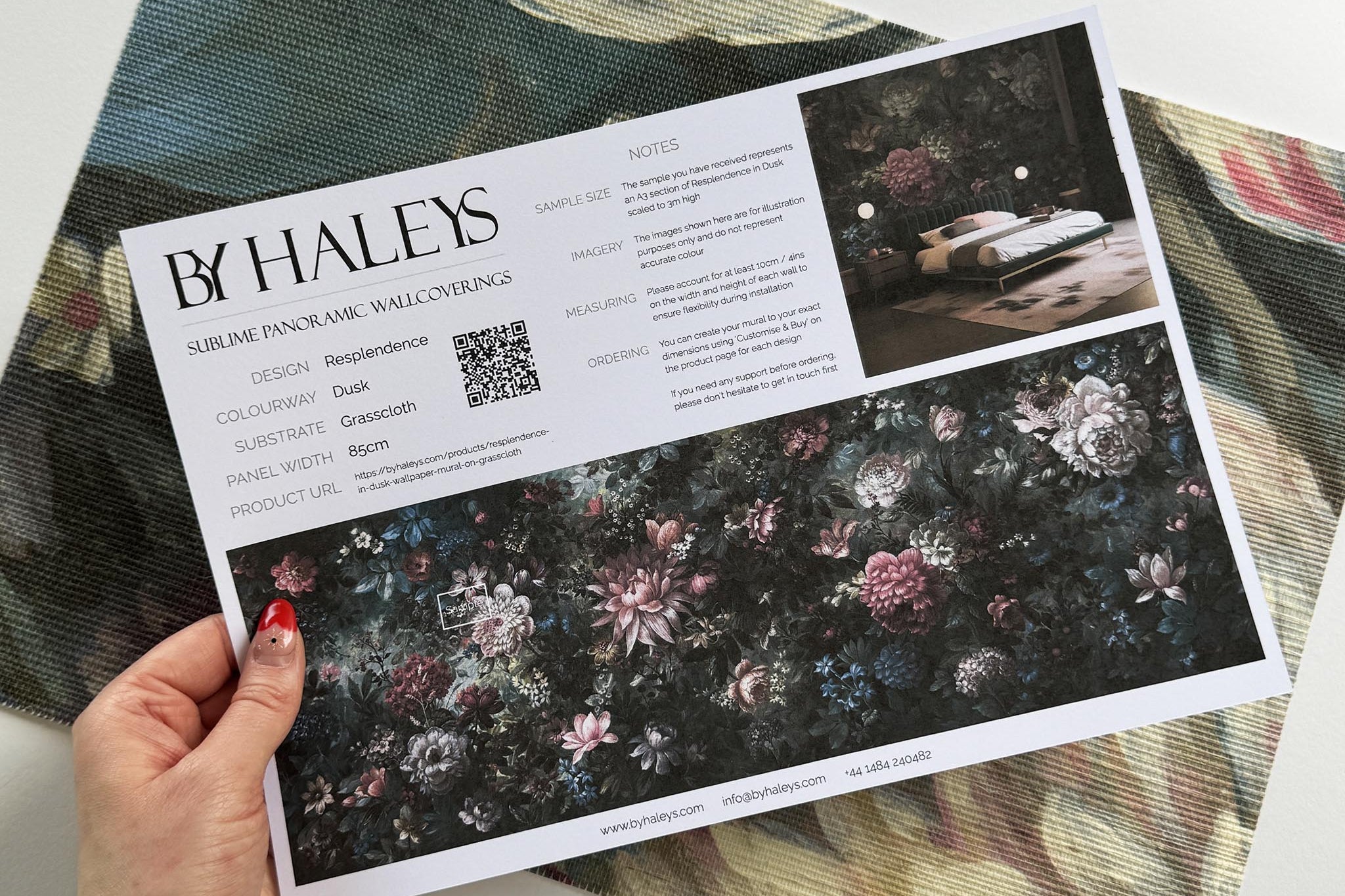 A hand showing information for a grasscloth wallpaper mural sample which features a floral bloom in crimson and blue.