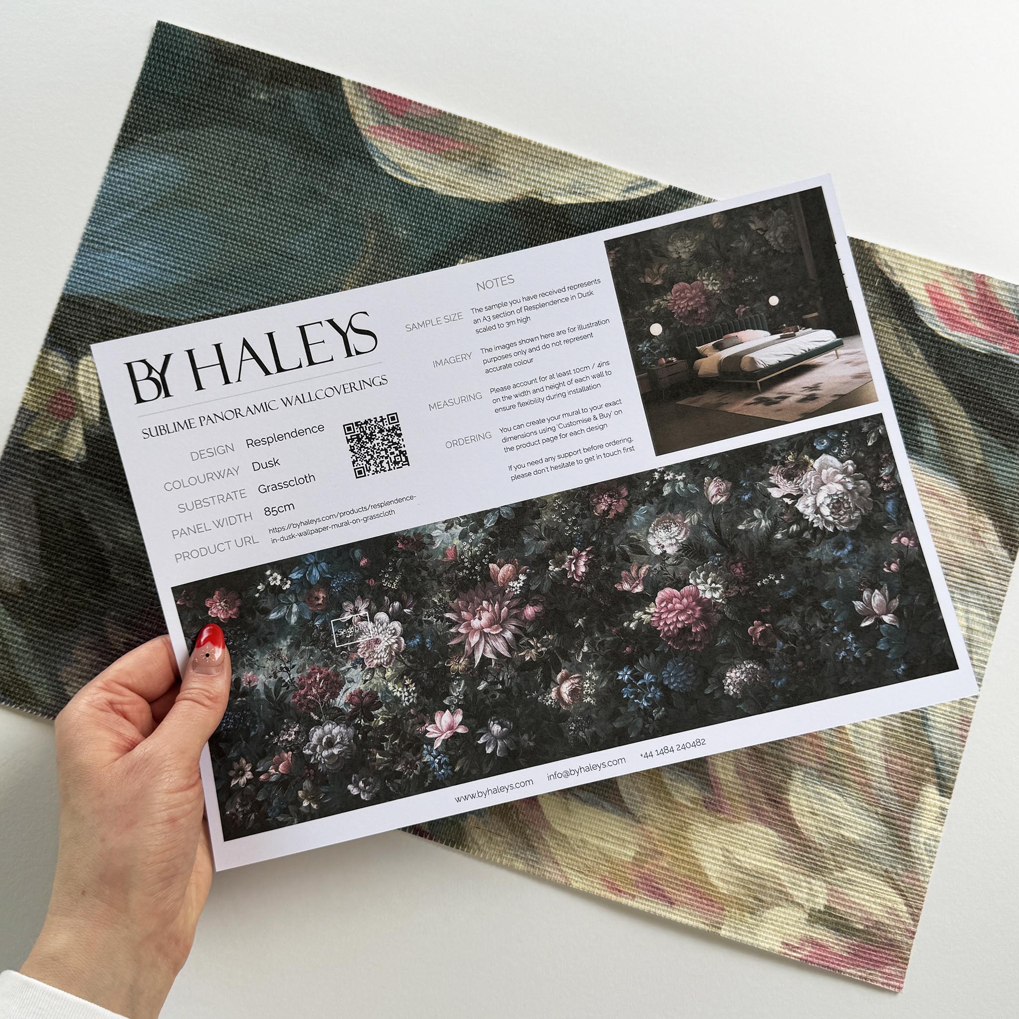 A hand showing information for a grasscloth wallpaper mural sample which features a floral bloom in crimson and blue.