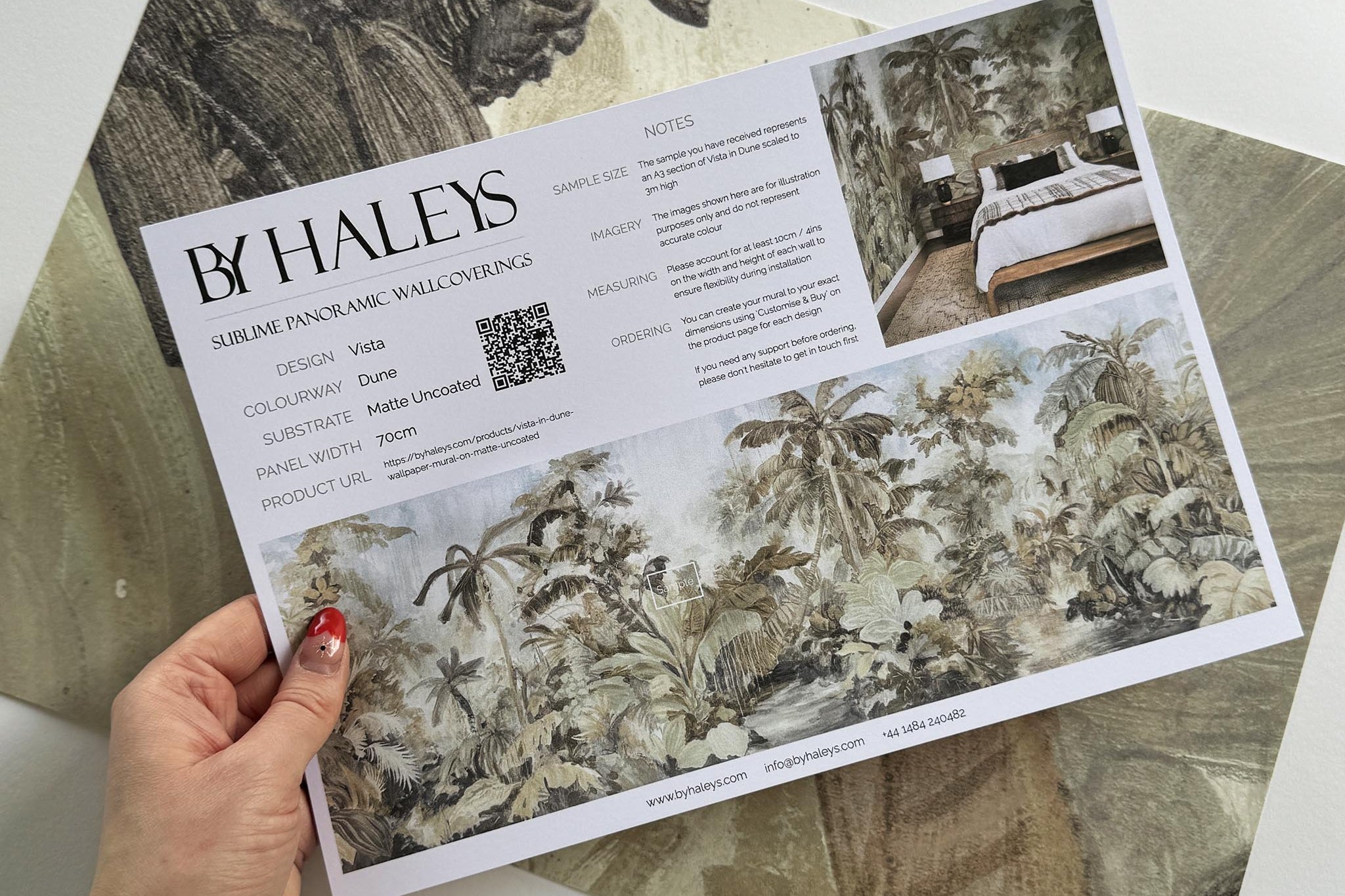 A hand showing information for a matte wallpaper mural sample which features a jungle scene in sepia and blue.