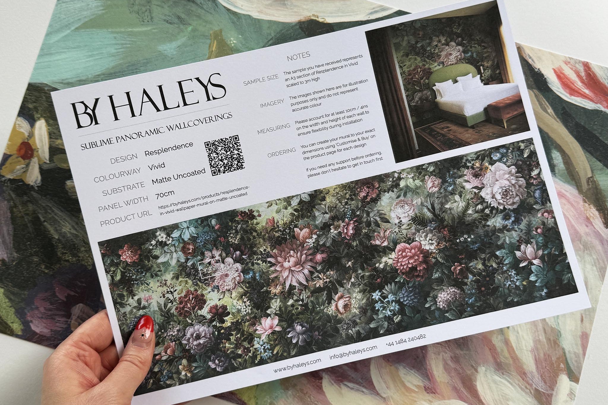 A hand showing information for a matte wallpaper mural sample which features a floral tapestry in rich jewel tones.