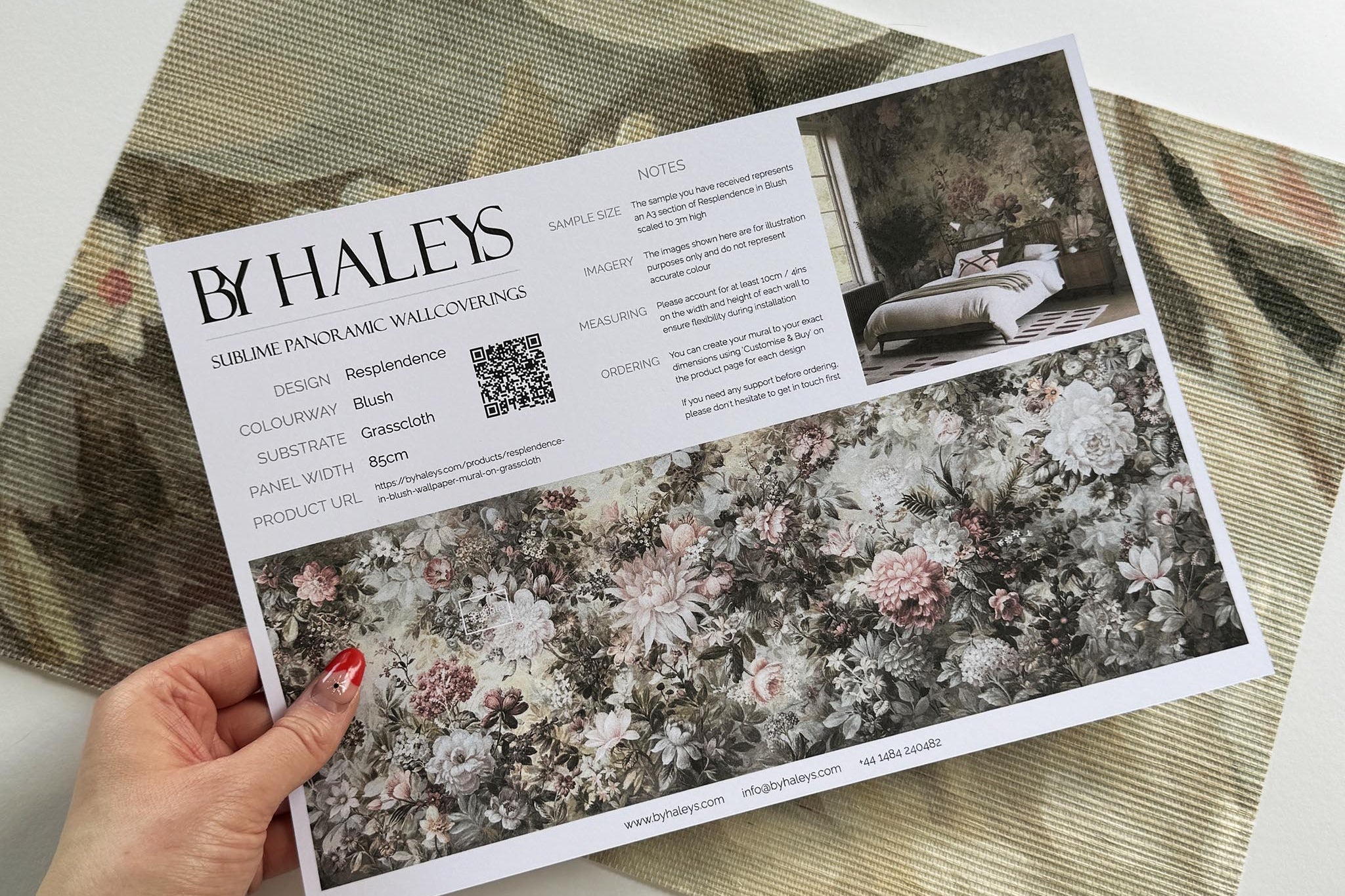 A hand showing information for a grasscloth wallpaper mural sample which features a floral composition in soft neutrals.
