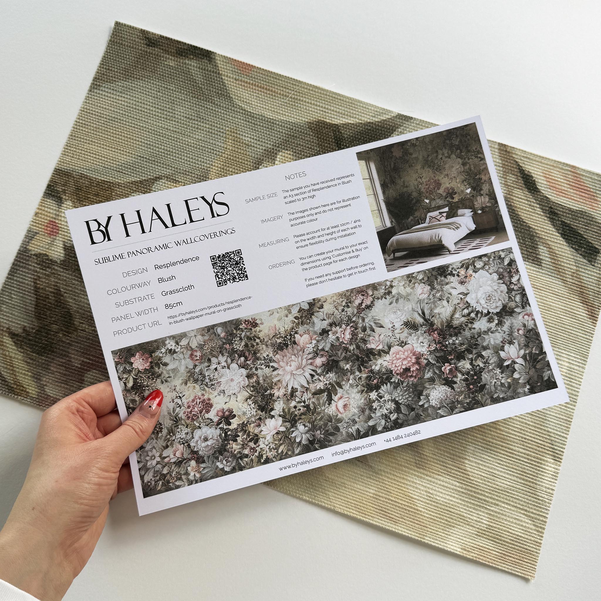 A hand showing information for a grasscloth wallpaper mural sample which features a floral composition in soft neutrals.