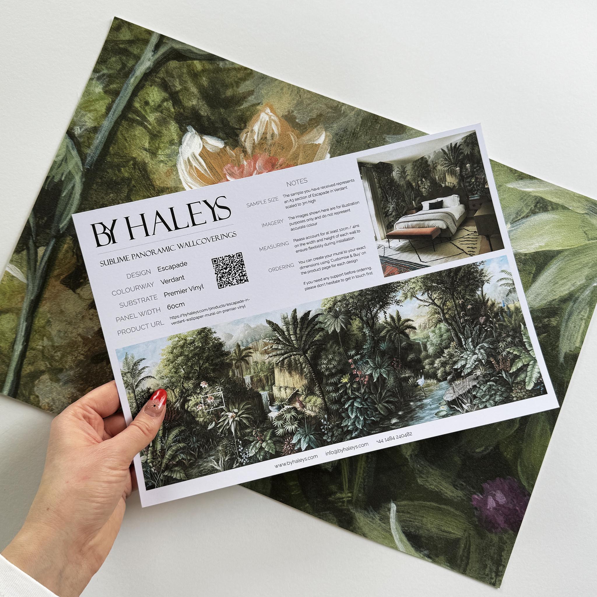 A hand showing information for a vinyl wallpaper mural sample which features a tropical scene in green and pink.