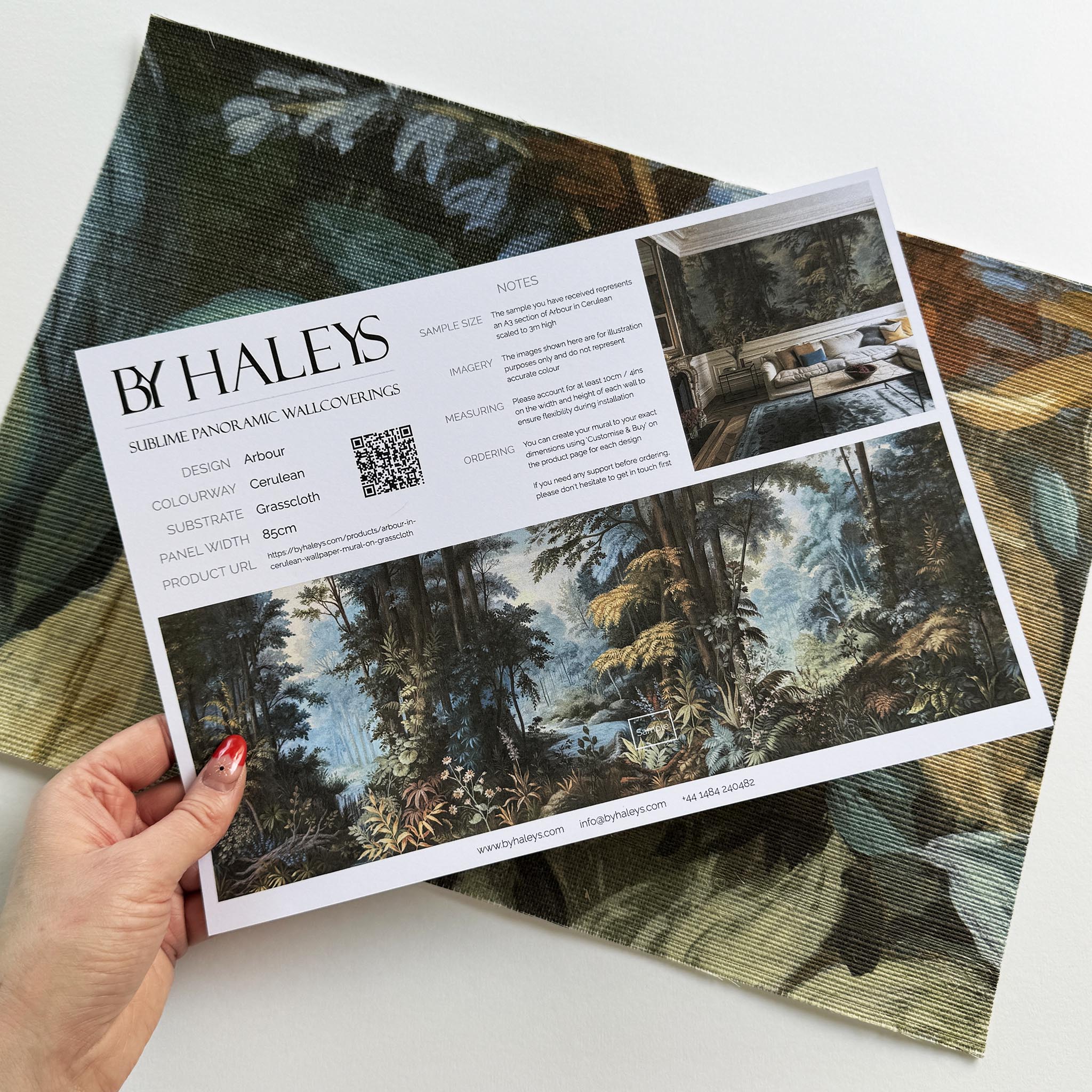 A hand showing information for a grasscloth wallpaper mural sample which features an enchanted forest in blue and rust.