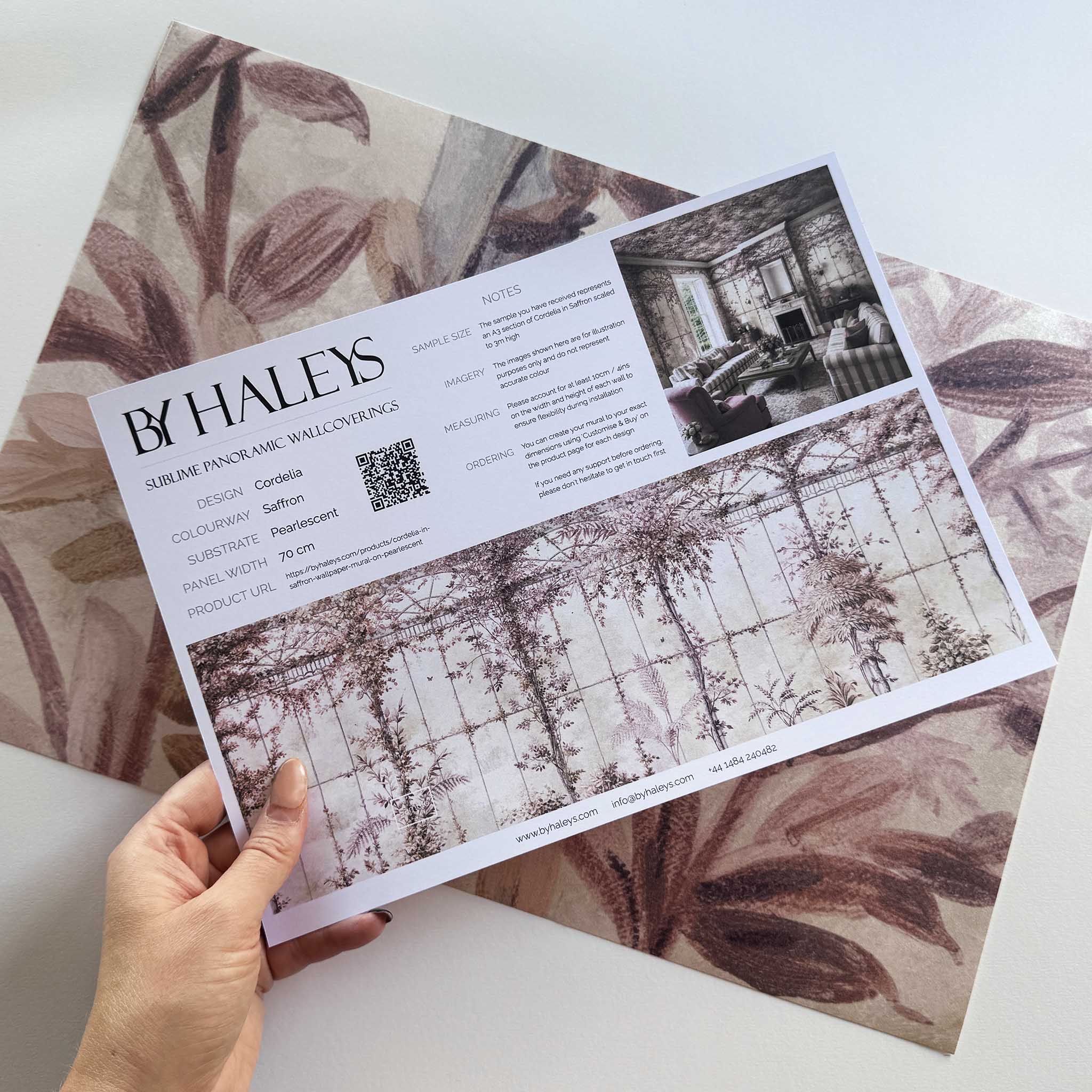 A hand showing information for a pearlescent wallpaper mural sample which features saffron toned mural with climbing foliage and vintage glass.