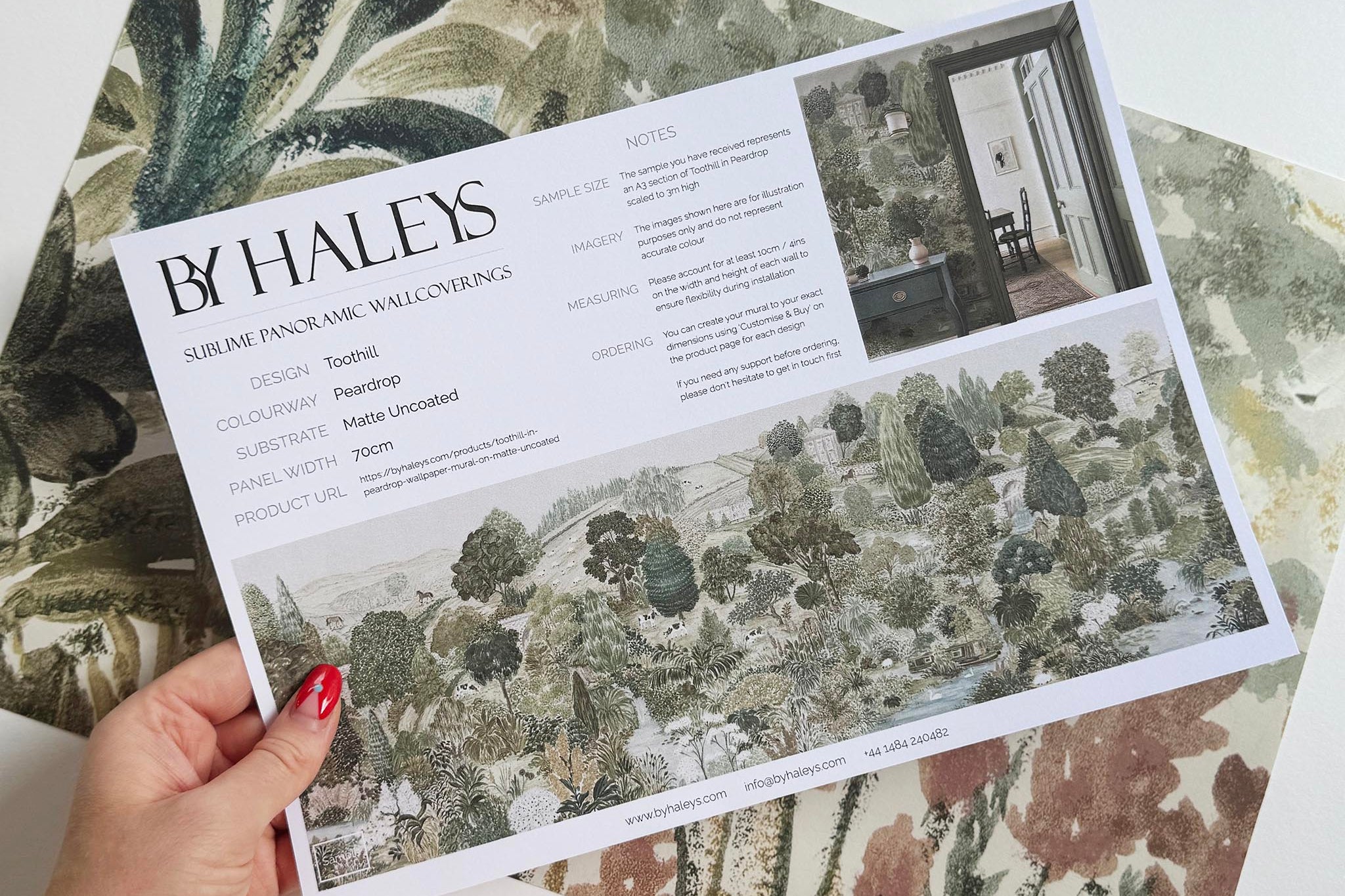 A hand showing information for a matte wallpaper mural sample which features a soft green countryside with cattle and boats
