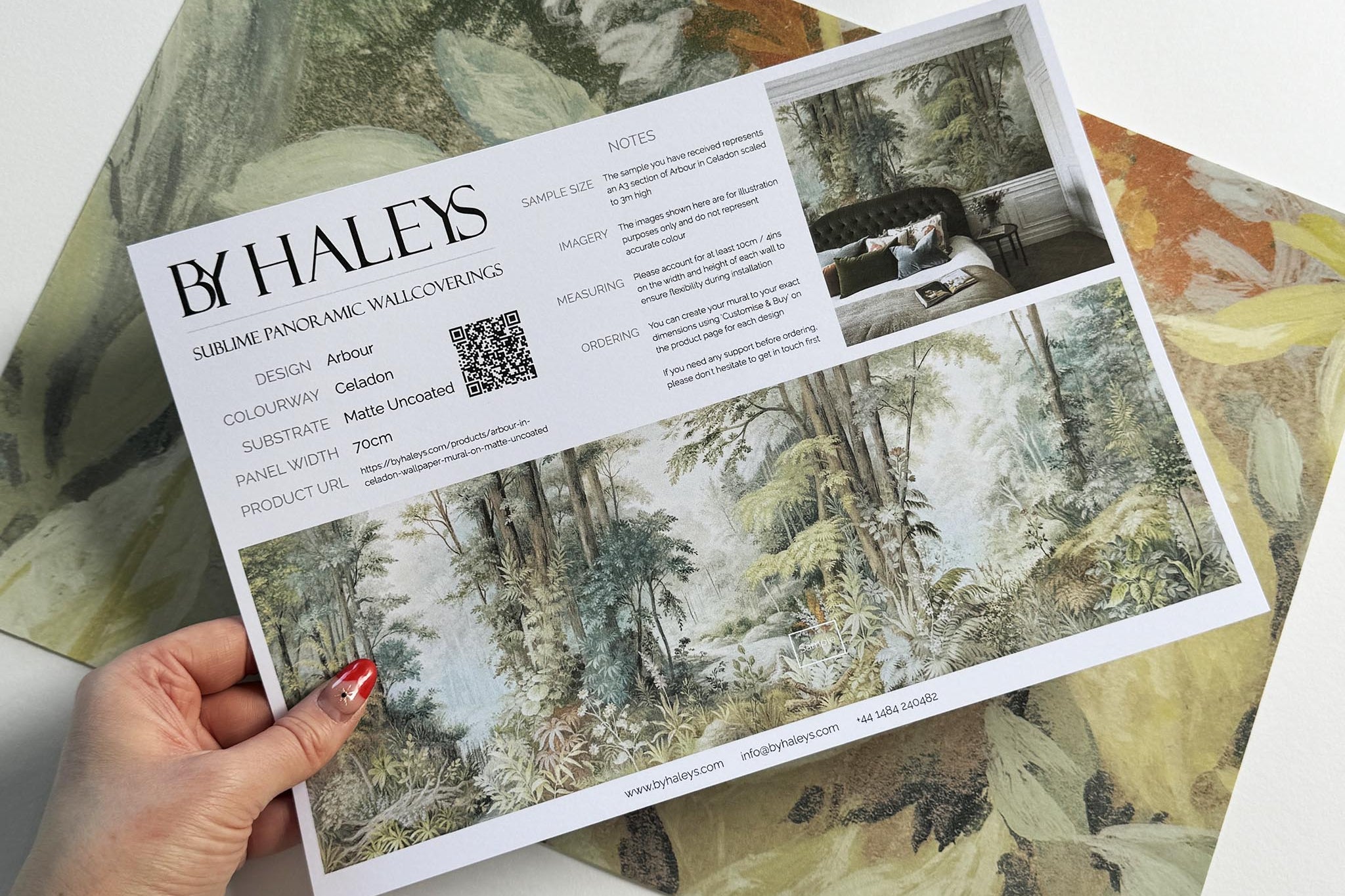 A hand showing information for a matte wallpaper mural sample which features an airy woodland in sage, yellow, and mist.