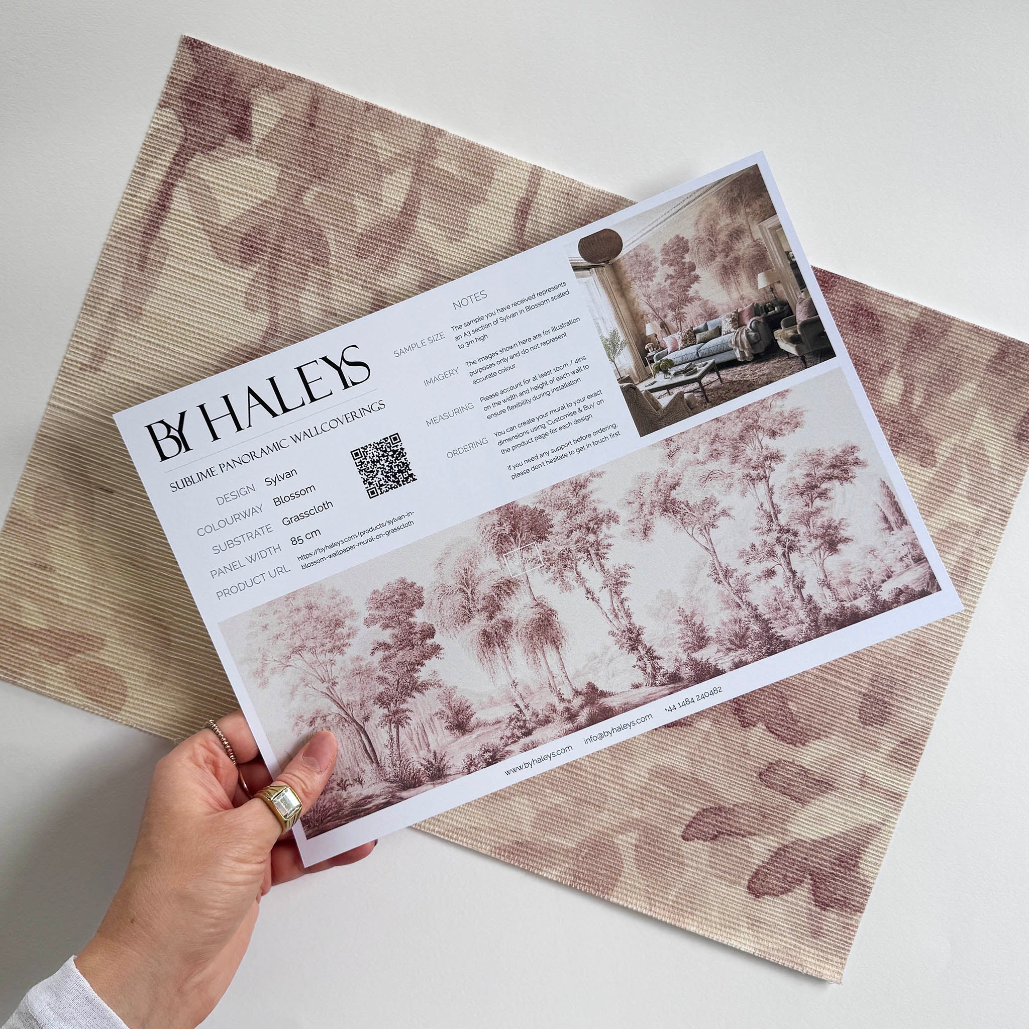 A hand showing information for a grasscloth wallpaper mural sample which features rose forest