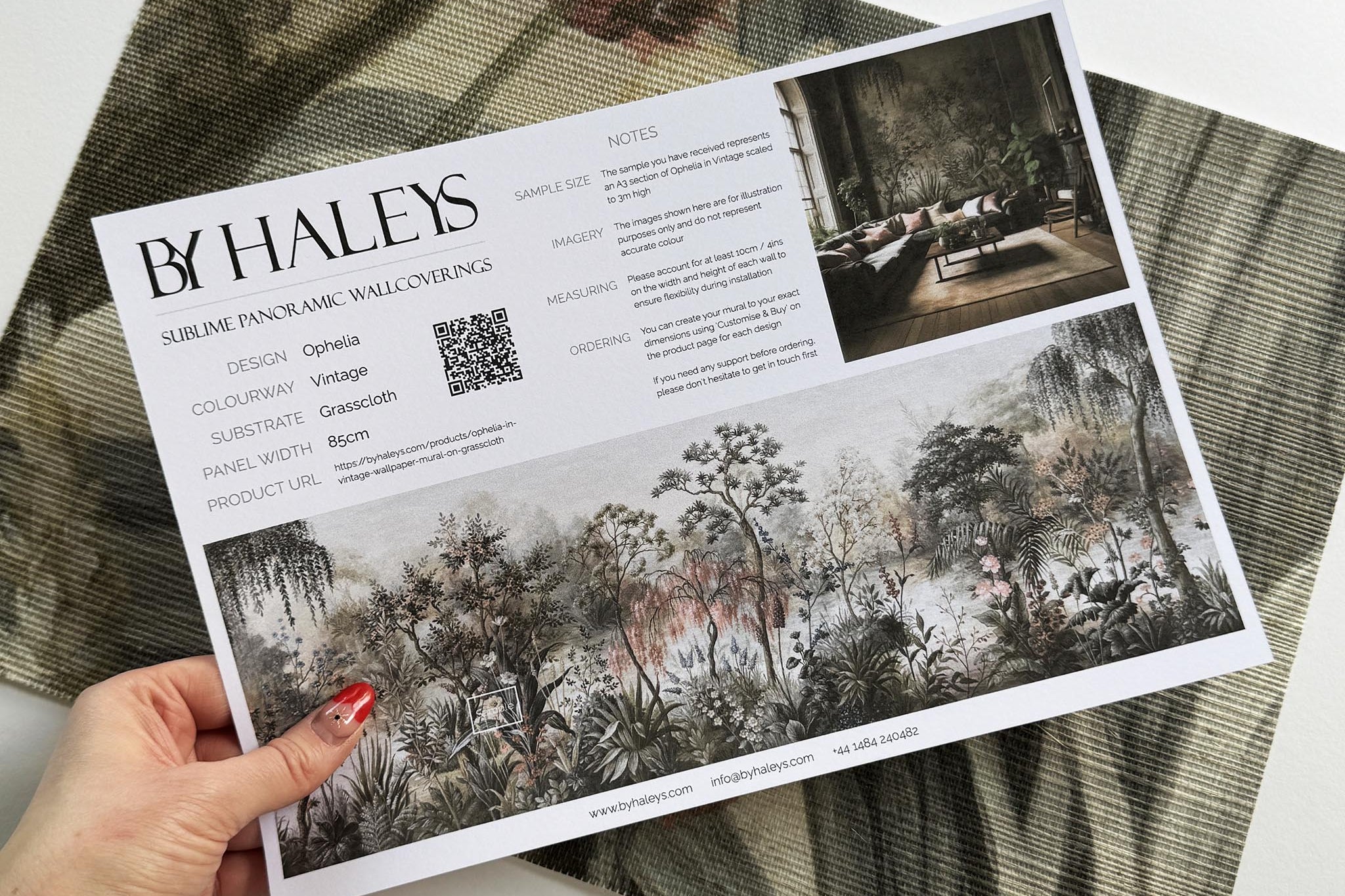 A hand showing information for a grasscloth wallpaper mural sample which features a lakeside scene in vintage tones.