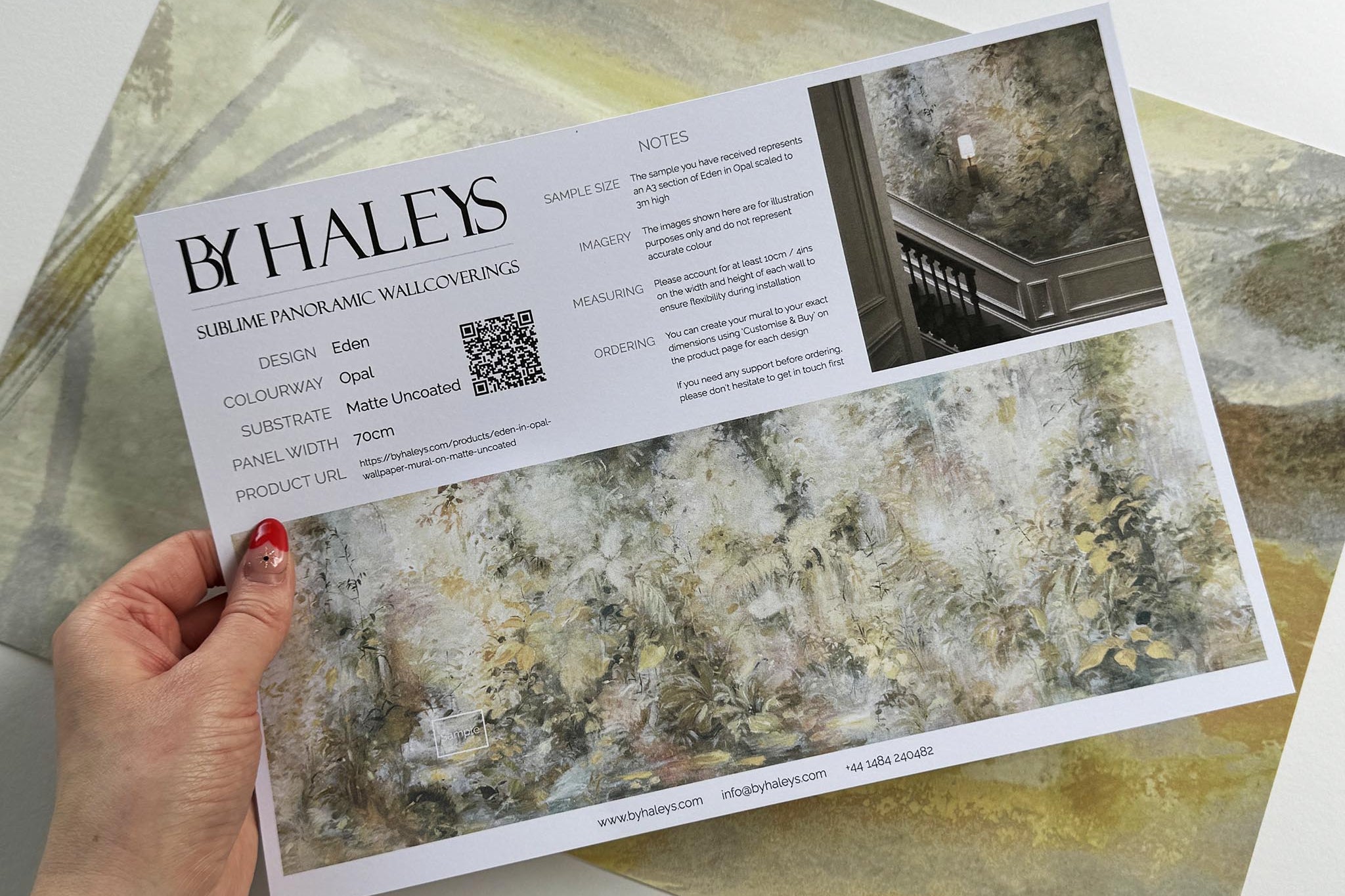 A hand showing information for a matte wallpaper mural sample which features an abstract forest in lemon and cream.