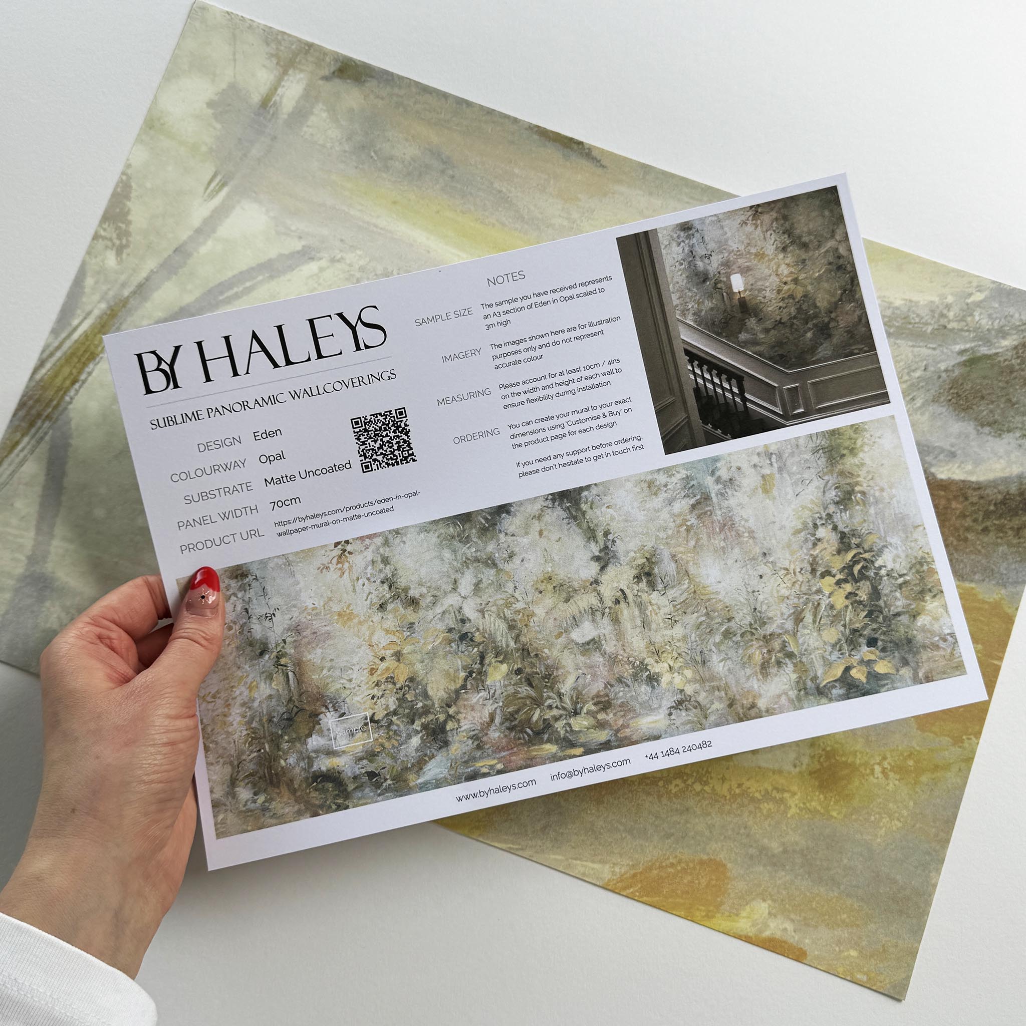 A hand showing information for a matte wallpaper mural sample which features an abstract forest in lemon and cream.