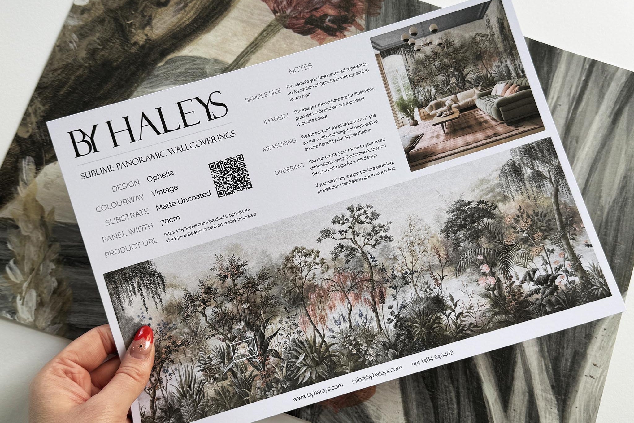 A hand showing information for a matte wallpaper mural sample which features a lakeside scene in vintage tones.