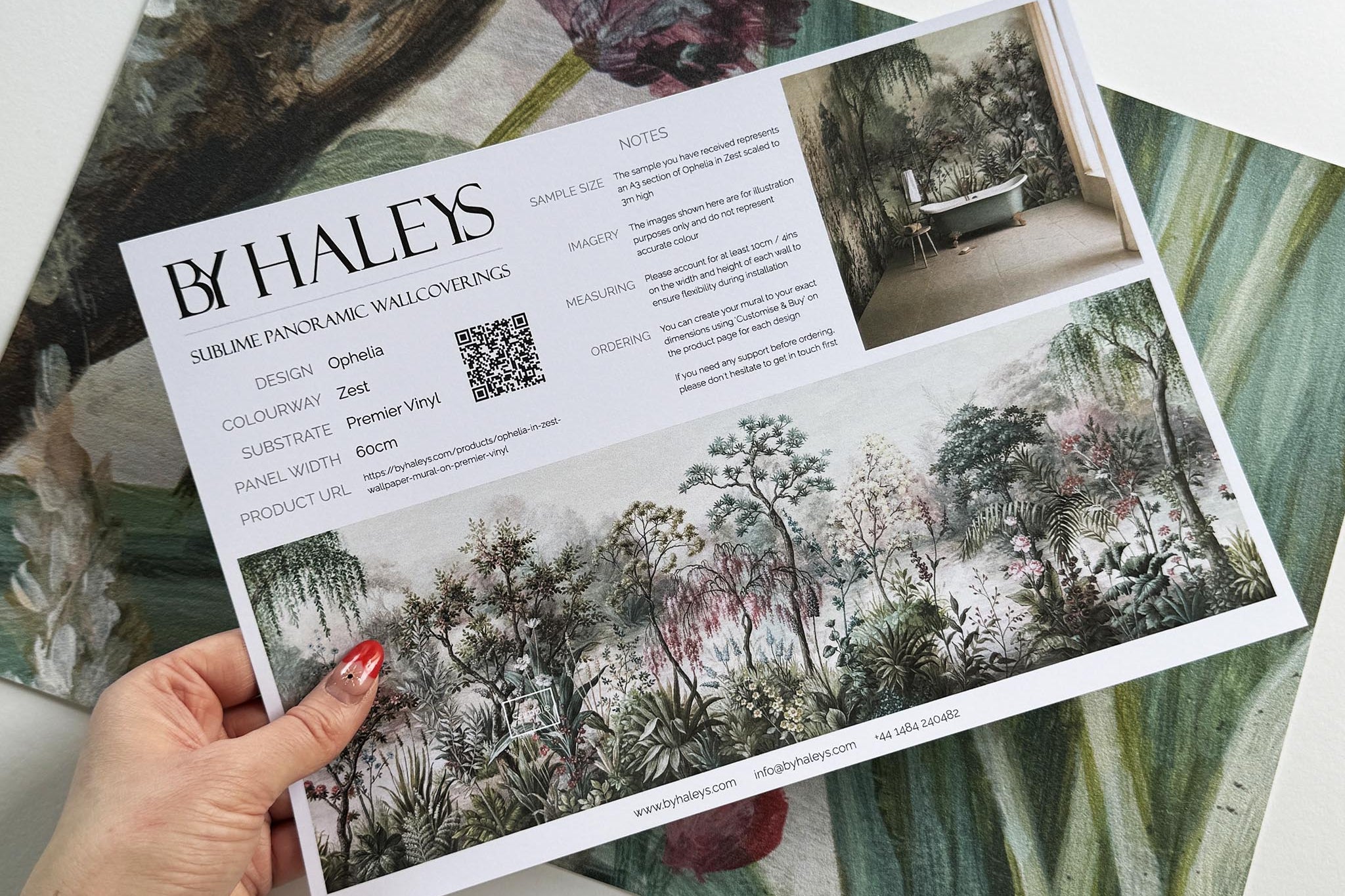 A hand showing information for a vinyl wallpaper mural sample which features a lakeside garden scene in mint and pink.